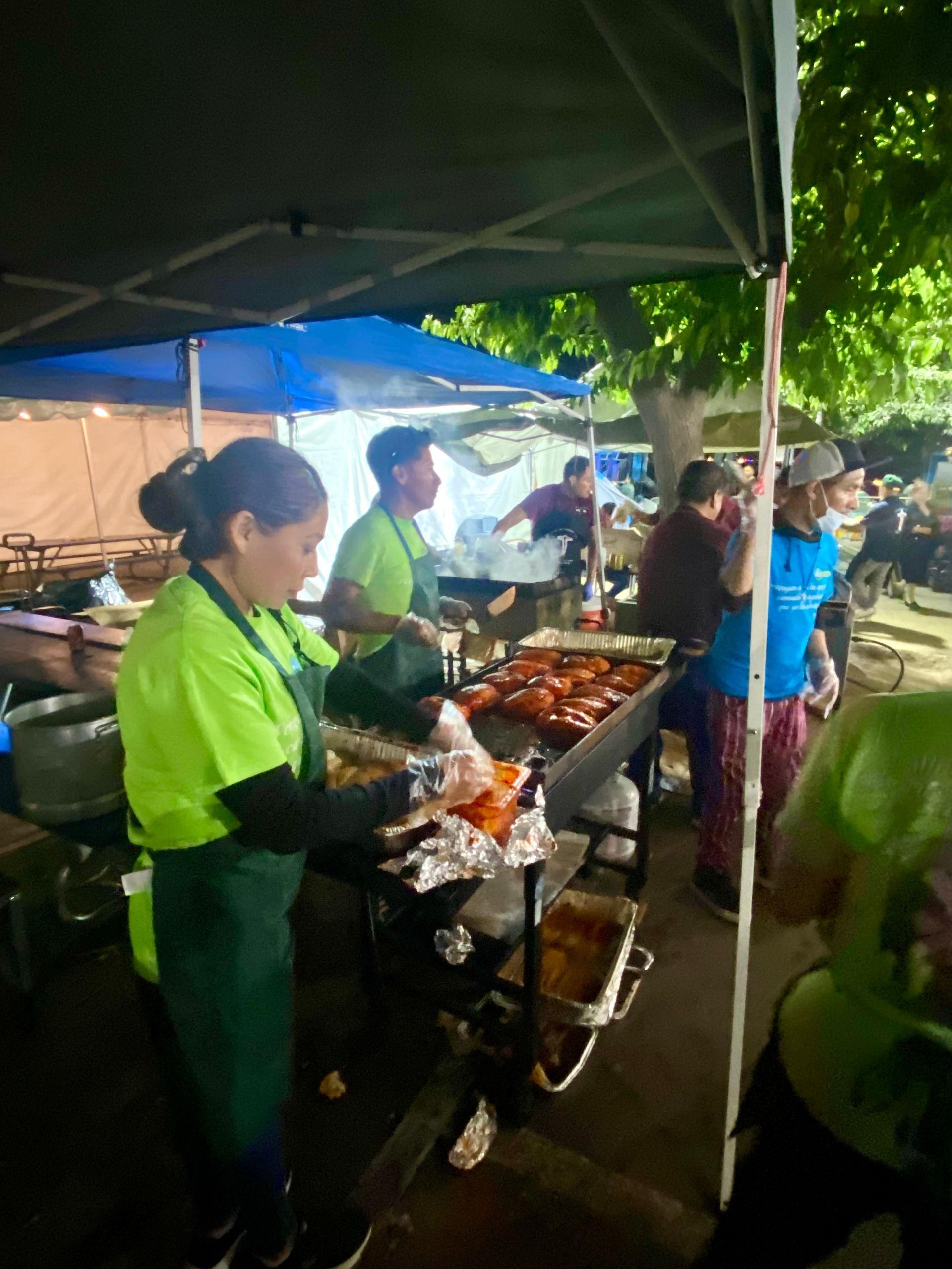 People serving grilled food at a nighttime outdoor market stall under tents