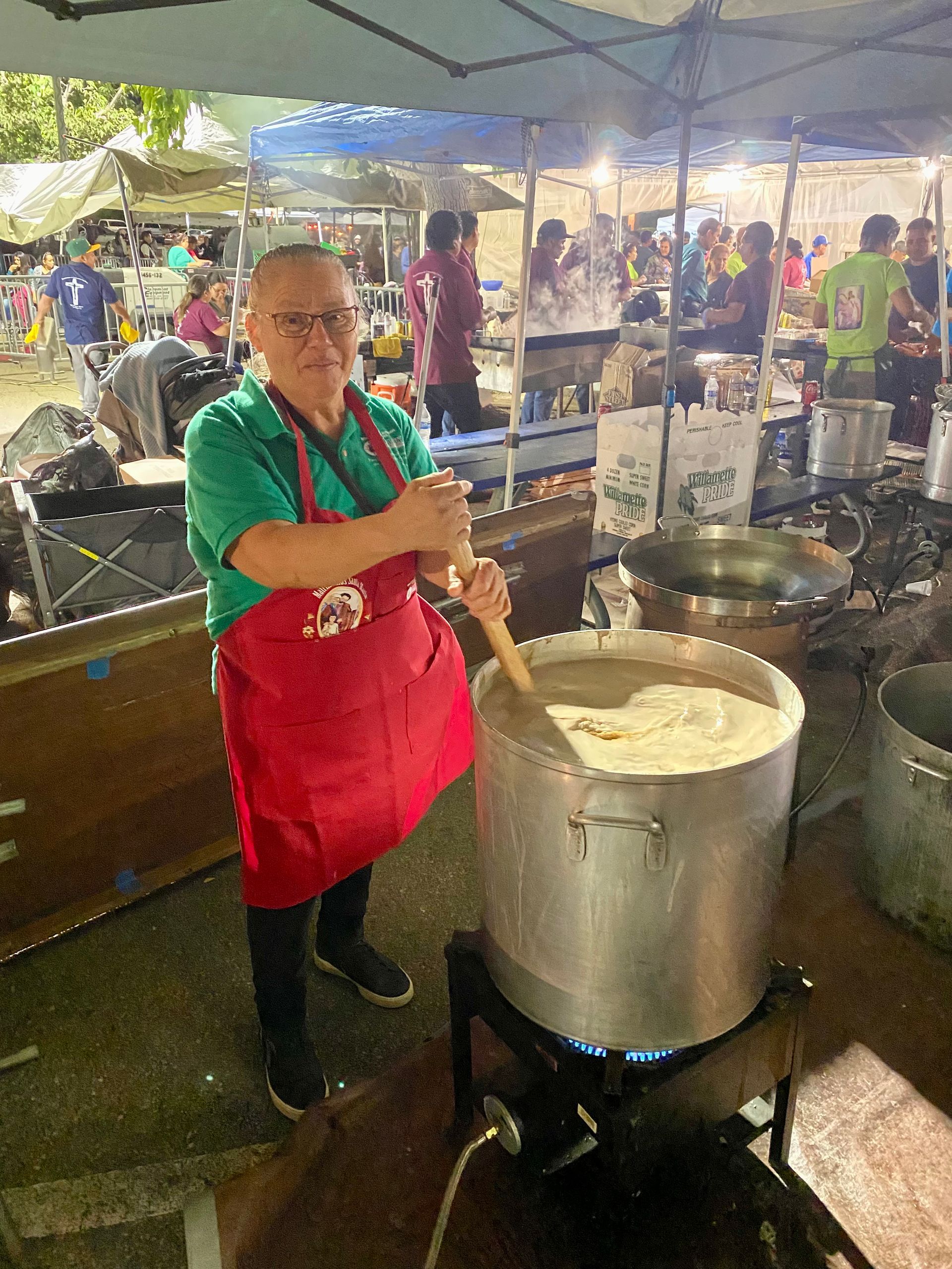 Street vendor stirring a large pot of food under a tent at an outdoor market