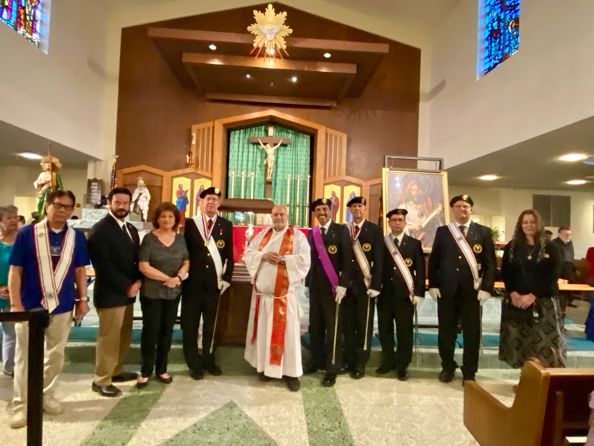 Group posed in a church aisle during a ceremony, with a robed clergy member at center.