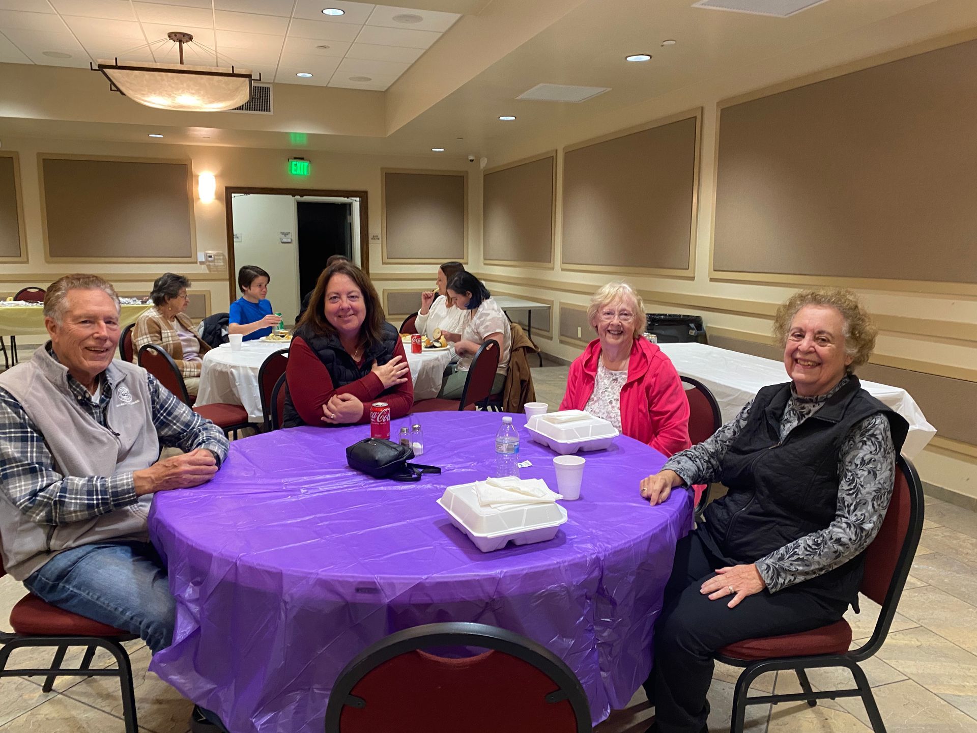 People seated around a purple tablecloth at a banquet table in a hotel meeting room