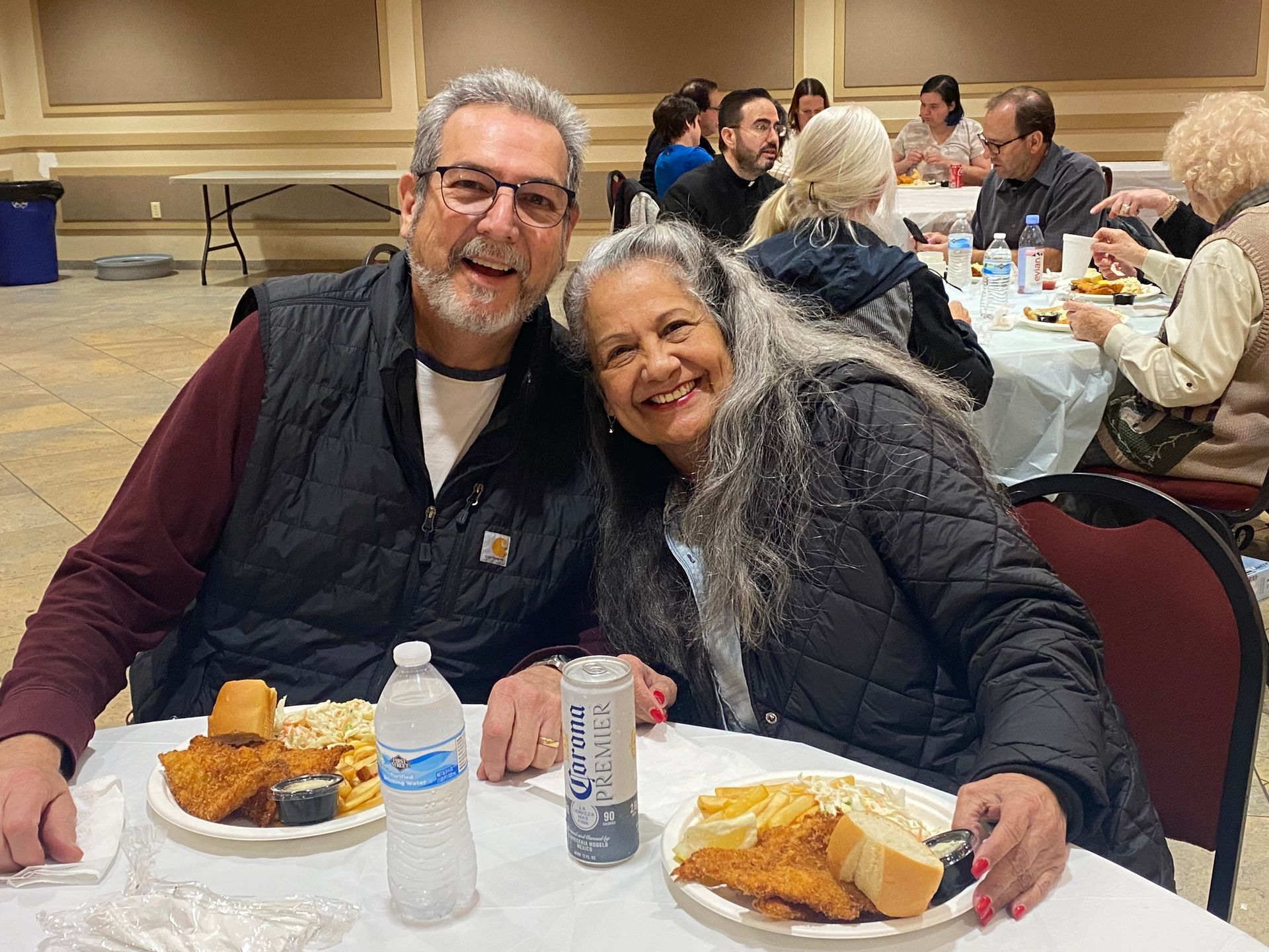 Two people smiling at a banquet table with plates of food and drinks in a banquet hall