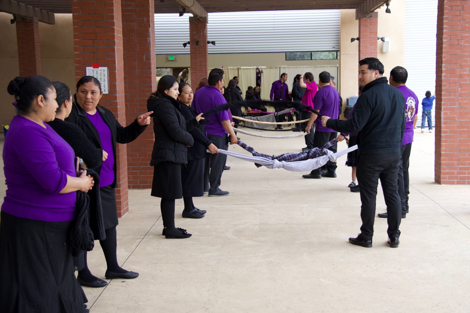 People in black and purple hold a rope line under a covered outdoor walkway.