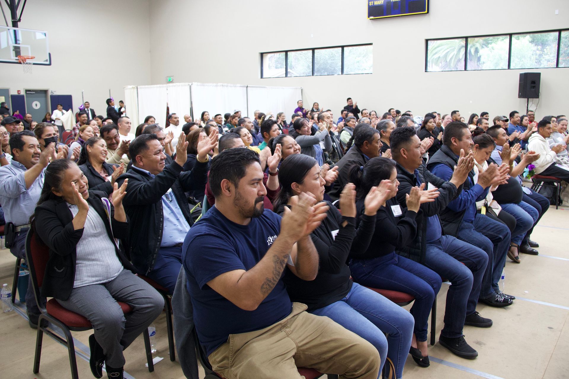 Audience seated indoors, clapping at a public event in a bright hall