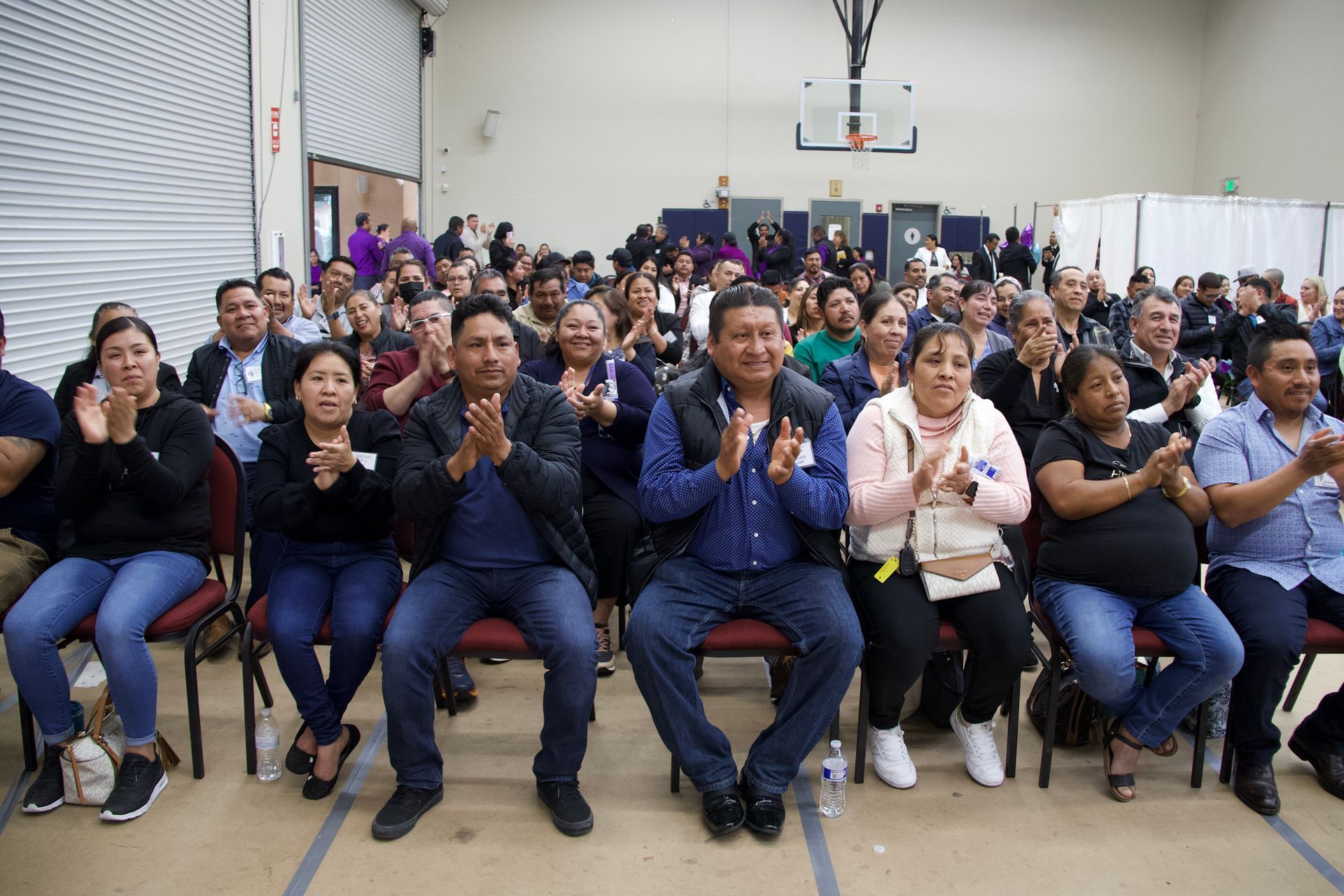 Crowd seated indoors clapping and smiling in a gymnasium