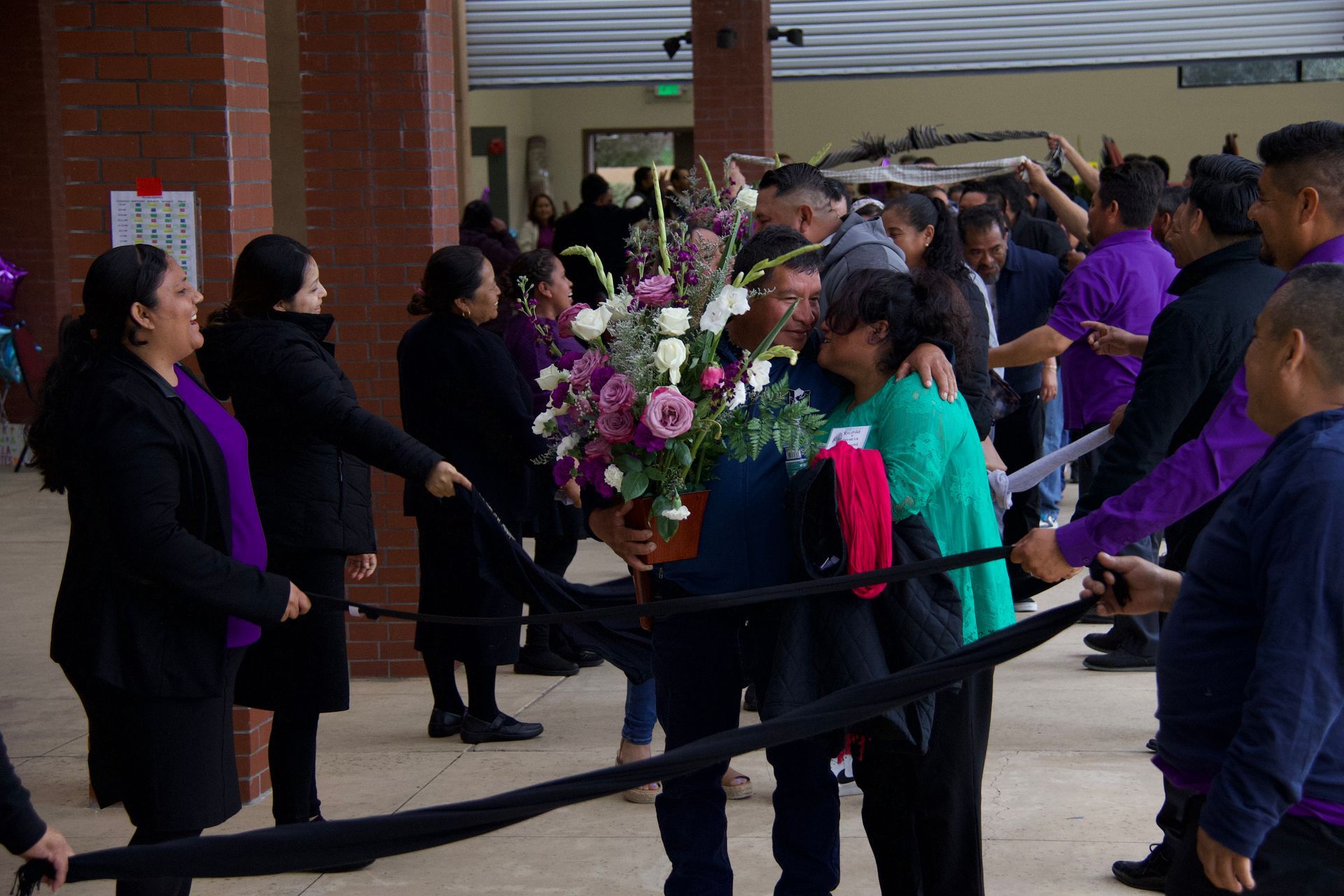 People holding a large floral wreath at an outdoor memorial gathering