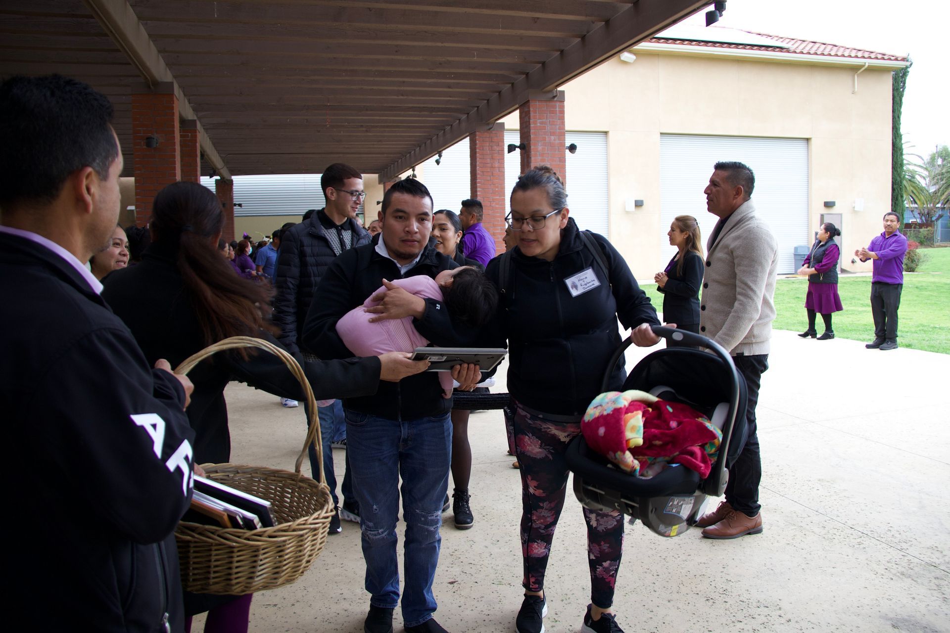 People exchanging baskets under a covered walkway, with others waiting nearby in an outdoor courtyard.