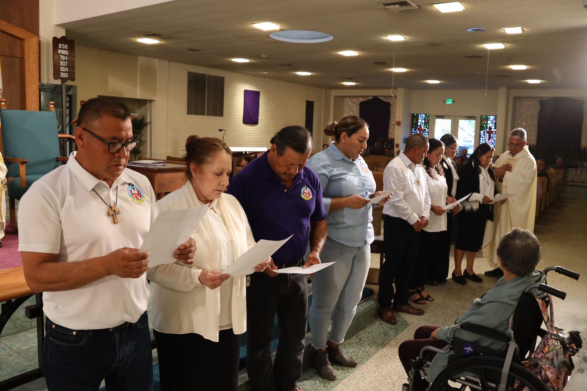 People standing in a hospital hallway holding papers, with a seated person nearby.
