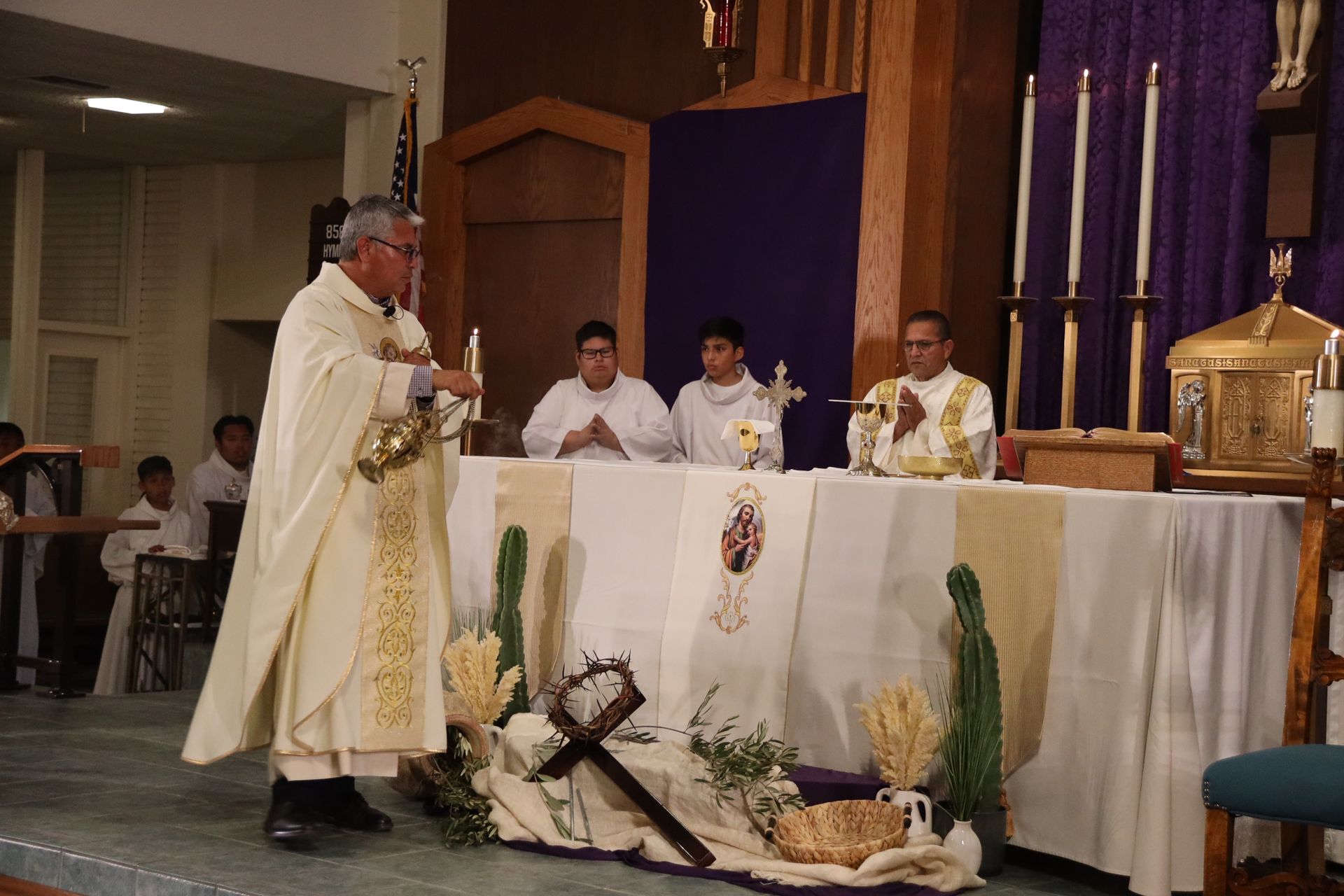 Priest at altar during church Mass, with other clergy and candles in a decorated sanctuary