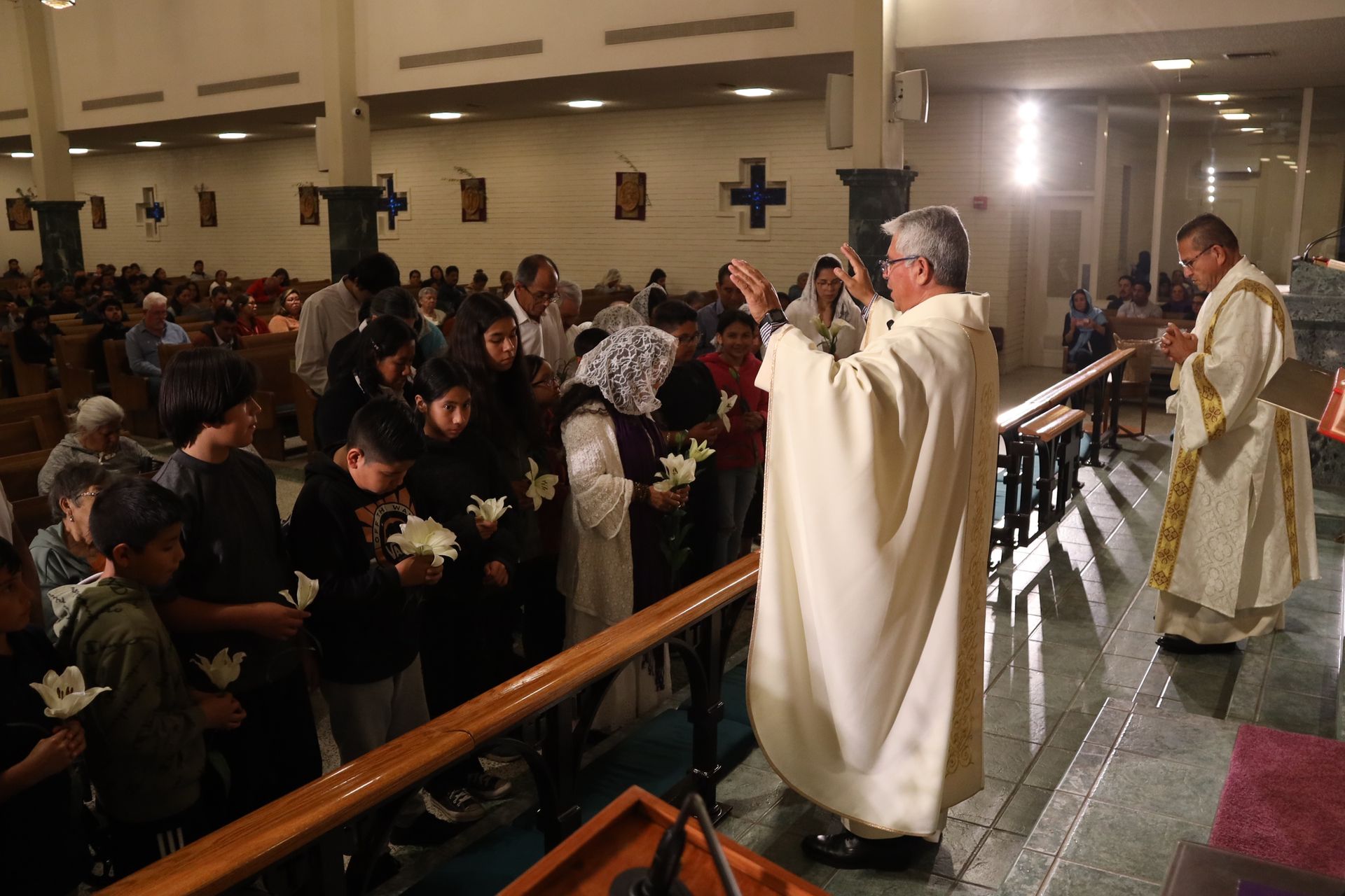 Priest in white robe blessing a crowded church congregation during a service