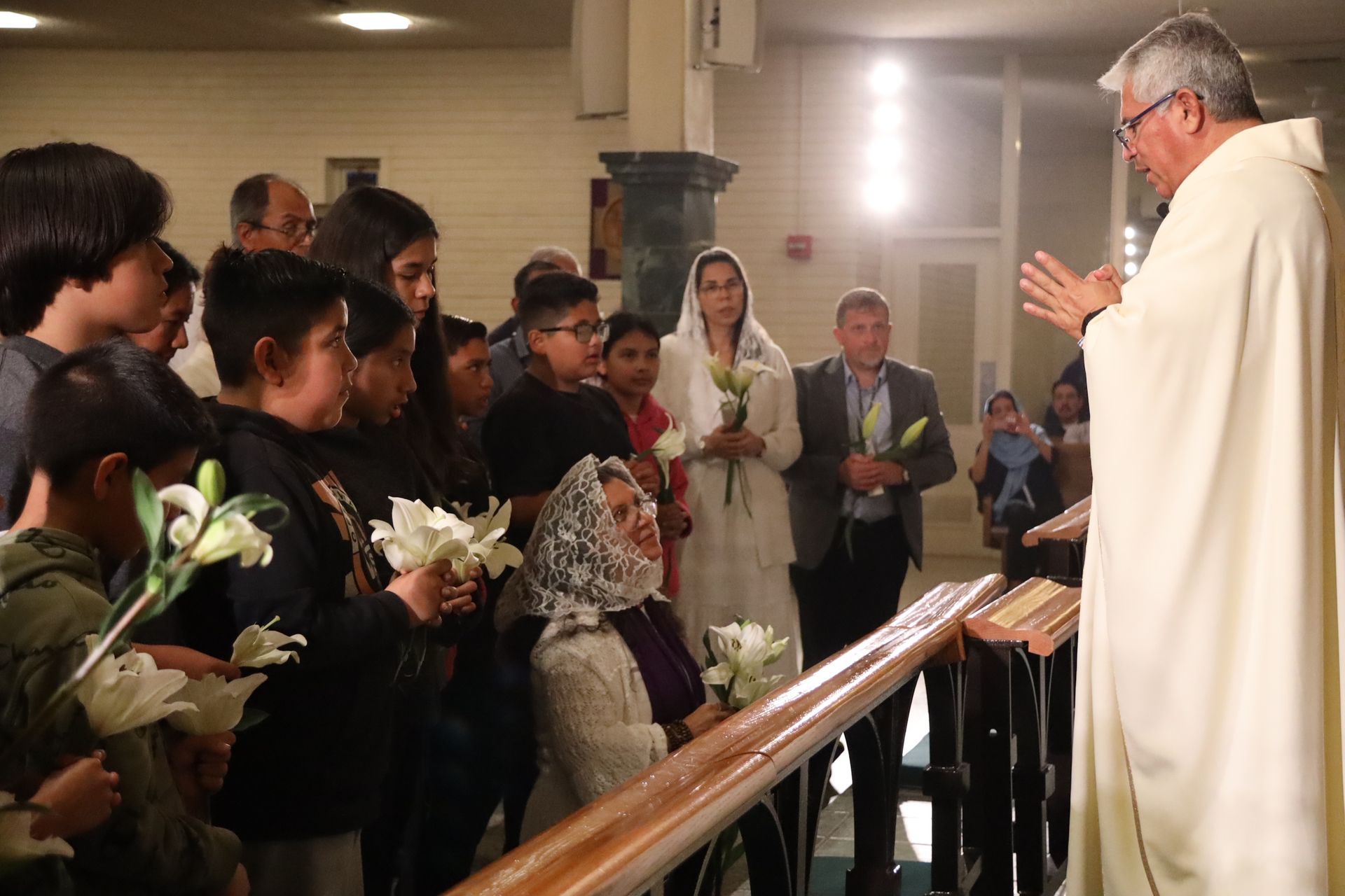 Priest blessing a line of people holding white flowers inside a church