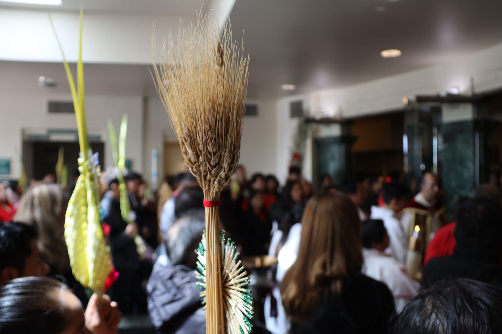 Crowded indoor event with tall floral arrangements in the foreground and people gathered in the background