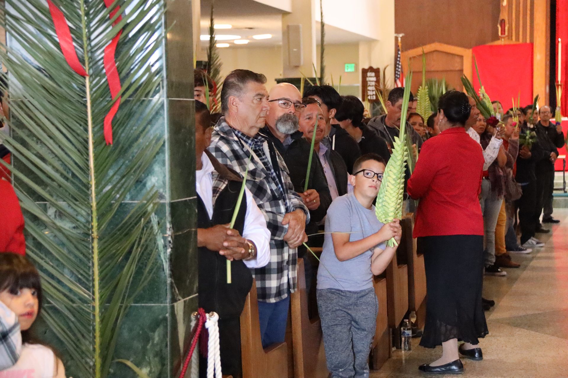 People standing in a line at an indoor event, holding items near a decorated entrance.