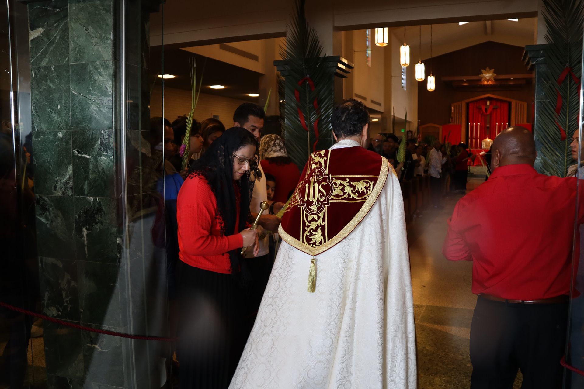 People entering a building, with a person in a white and red ceremonial cape in the foreground