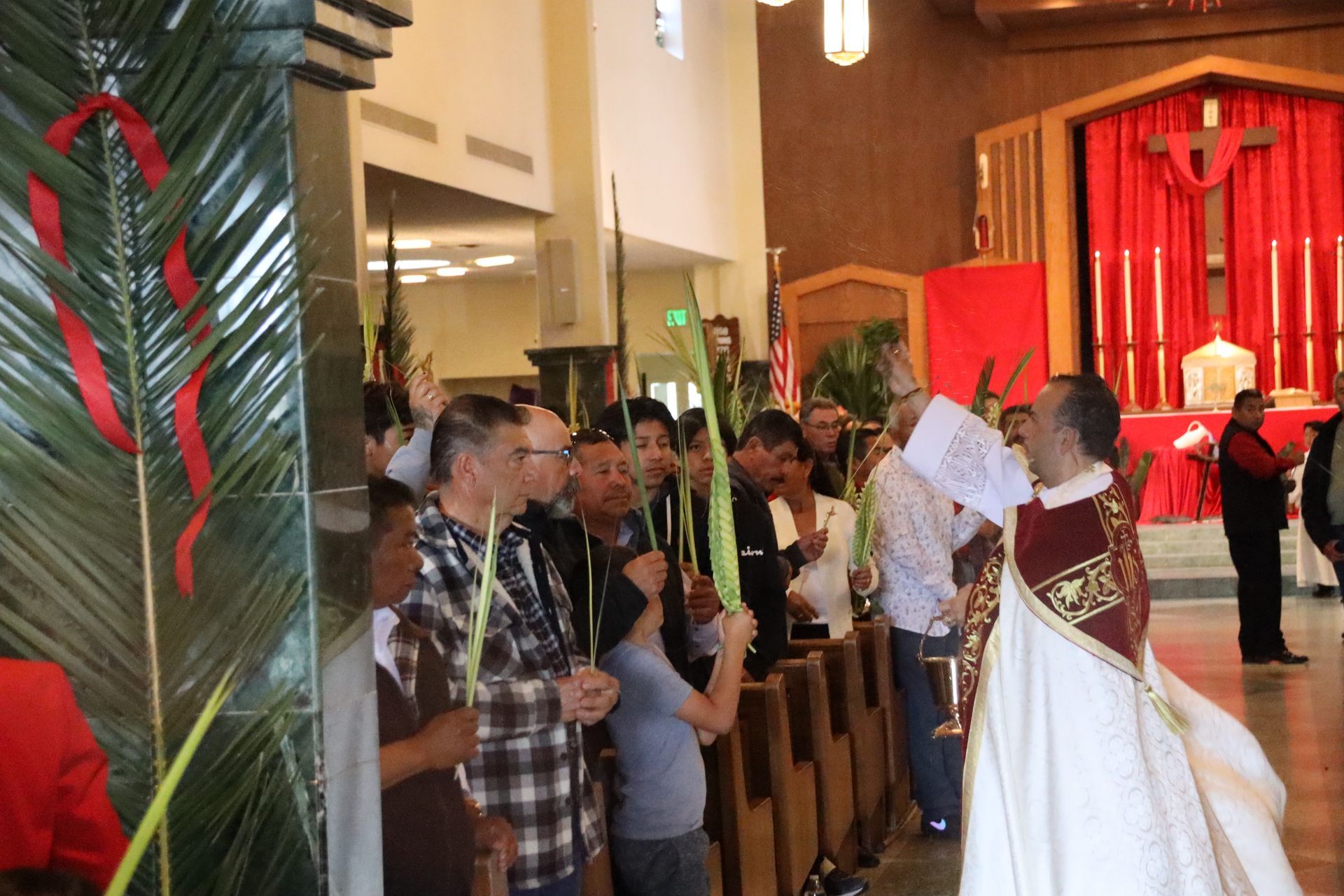 Crowd at a church ceremony receiving palm fronds from a priest in white robes