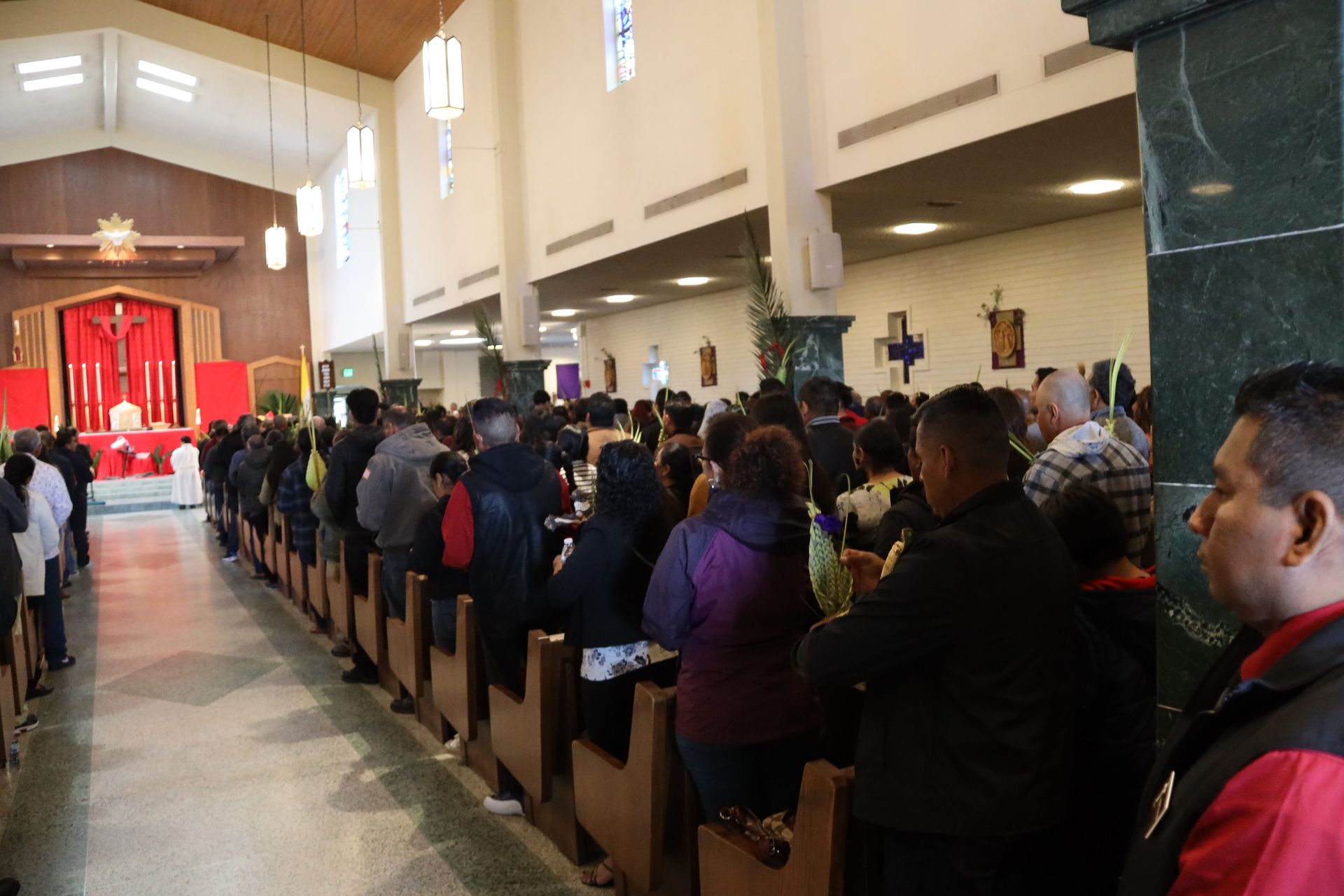 Congregants seated in a church pew, facing a red altar at the front of a bright sanctuary.