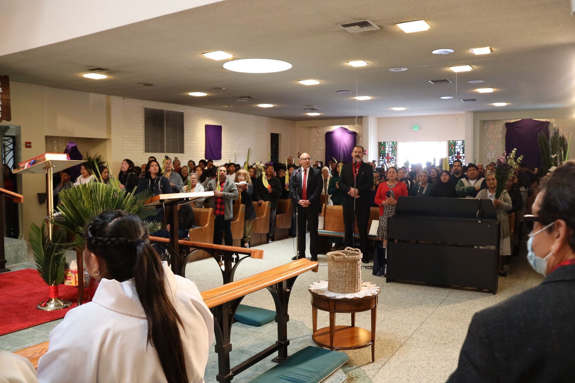 Indoor gathering with people standing around a central table and podium in a decorated hall