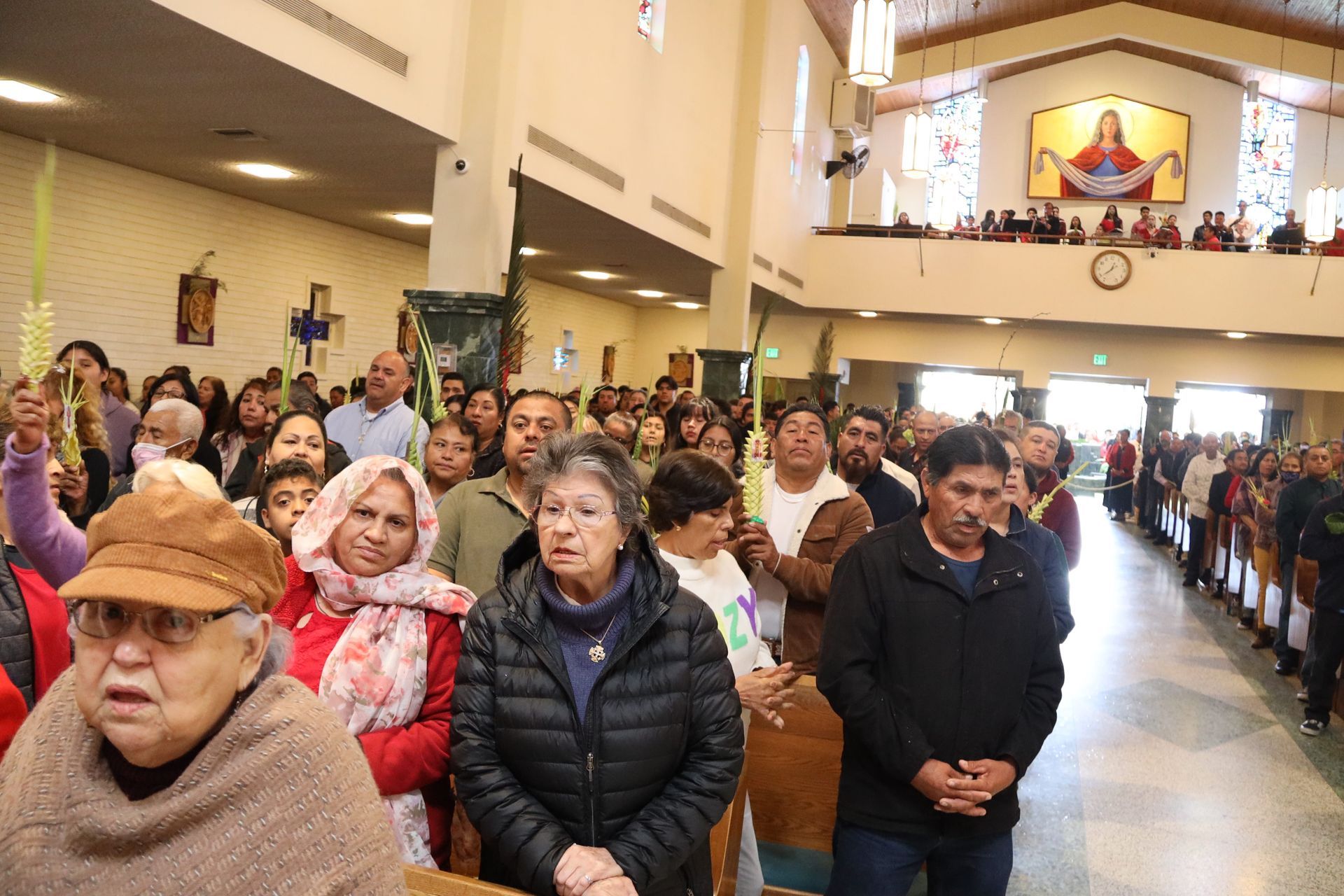 People standing in a church aisle during a crowded service, facing forward in winter clothing.