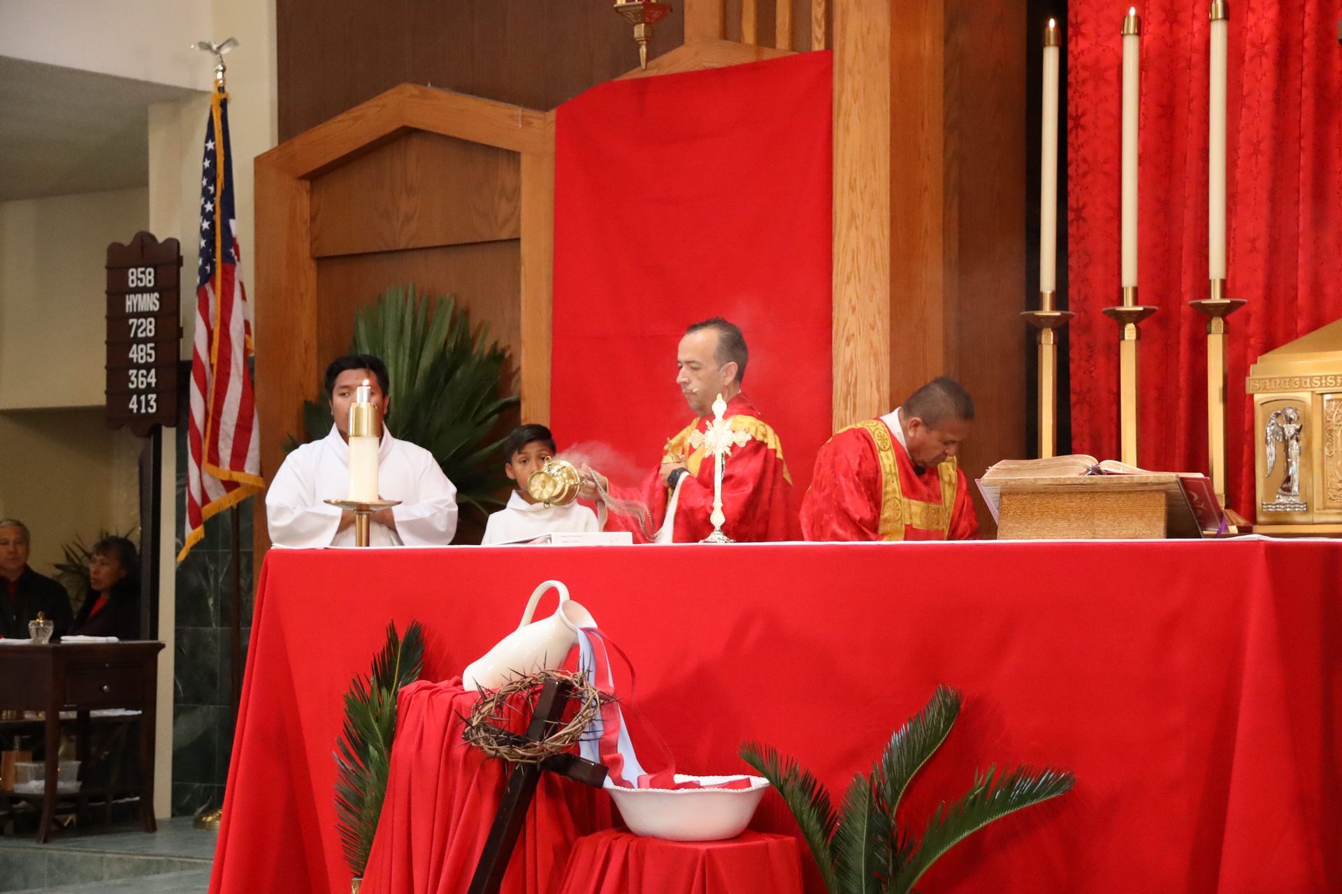 Priests officiate at a red-draped altar with candles in a church or temple.