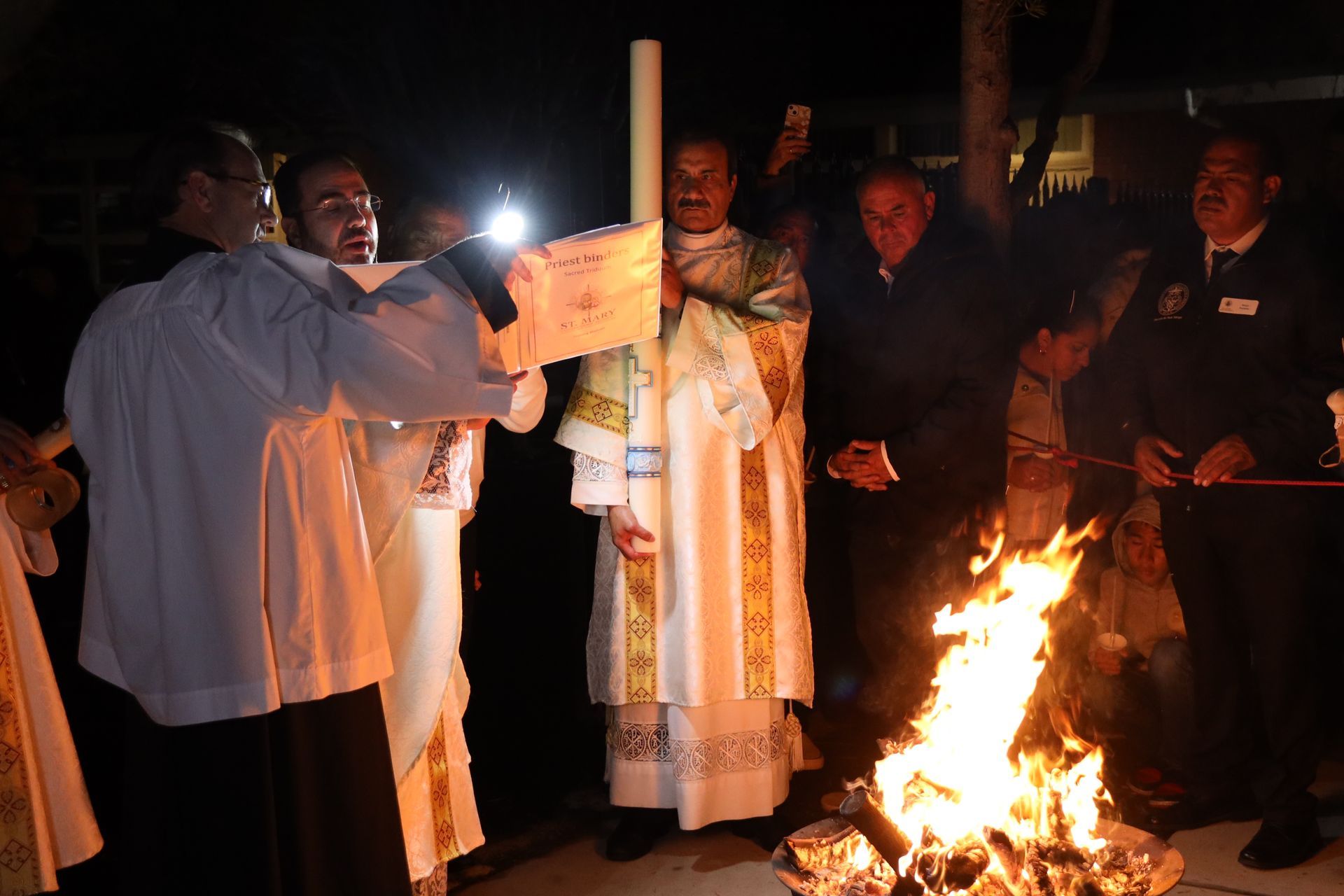 Priest blessing a candlelight ceremony beside a fire at night