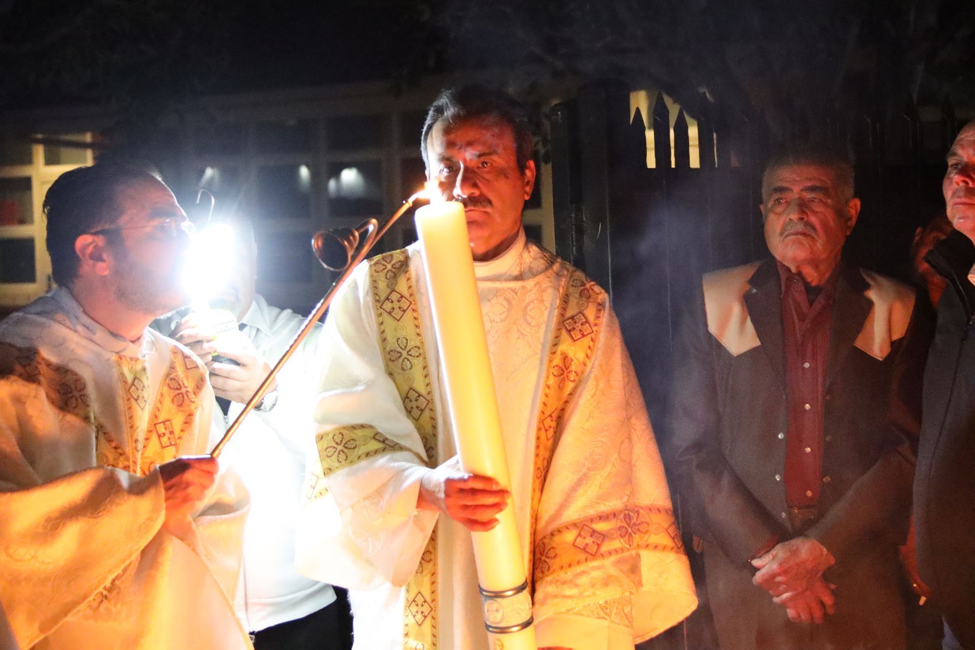 Three people in ceremonial robes holding candles at a nighttime service