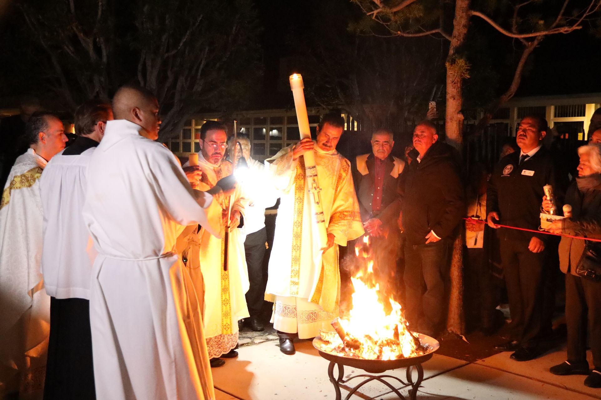 People in white robes gather around a small fire at night during a ritual outdoors.