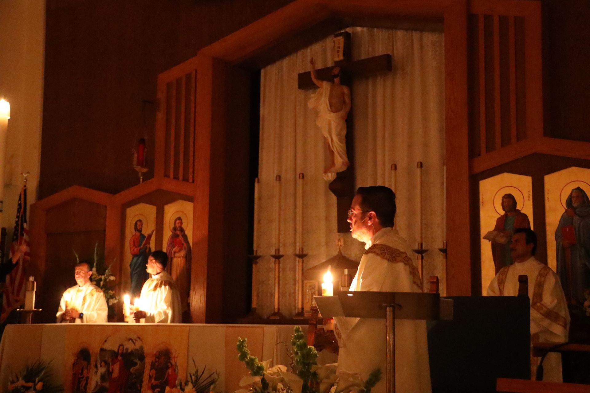 Candles lit on a church altar during a religious ceremony, with people standing nearby