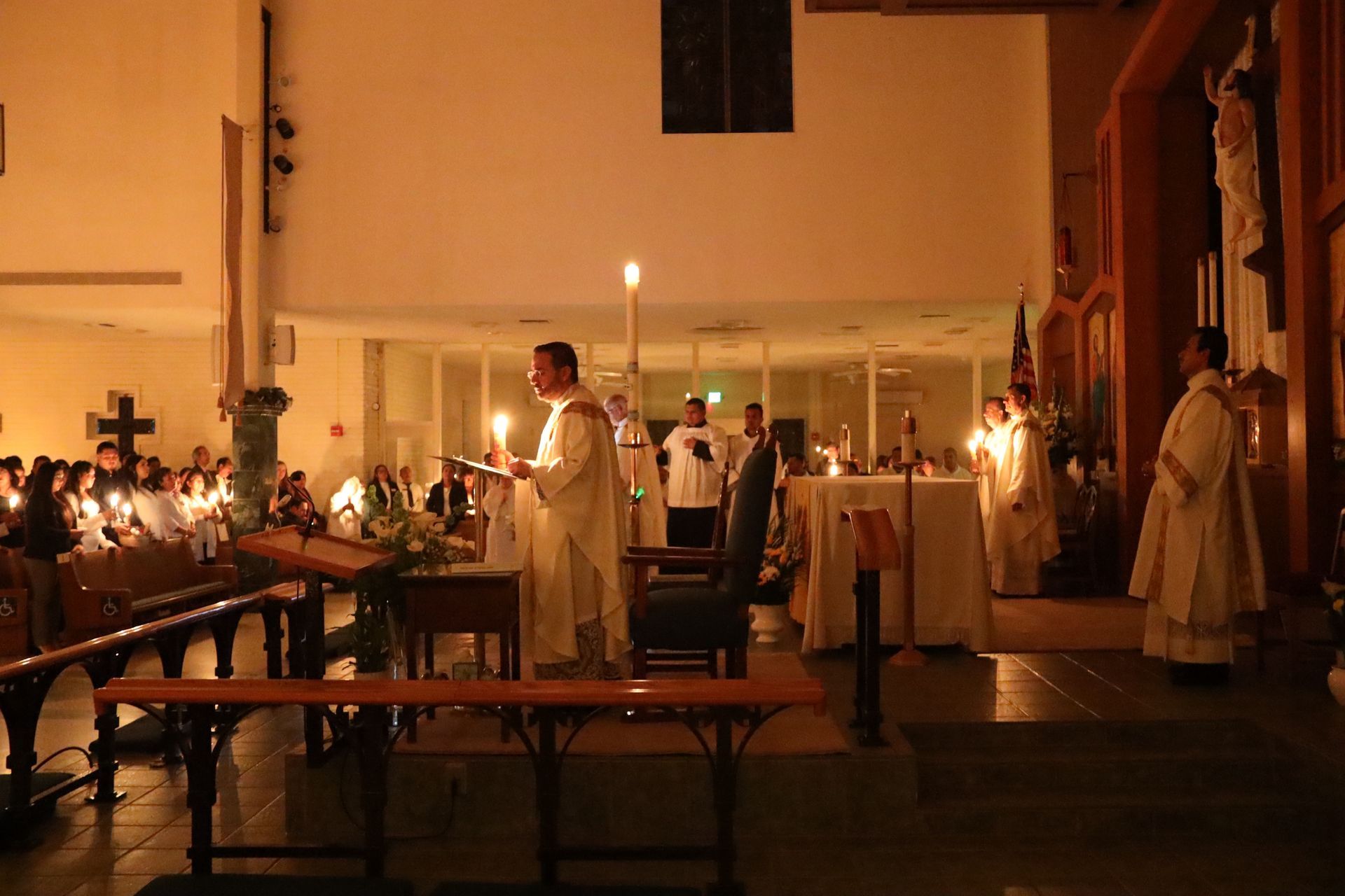 People in white robes gathered by candlelight inside a church during a solemn ceremony