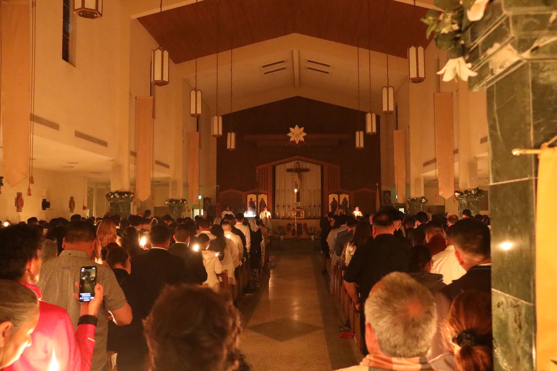 Dimly lit church aisle crowded with people holding candles during a service