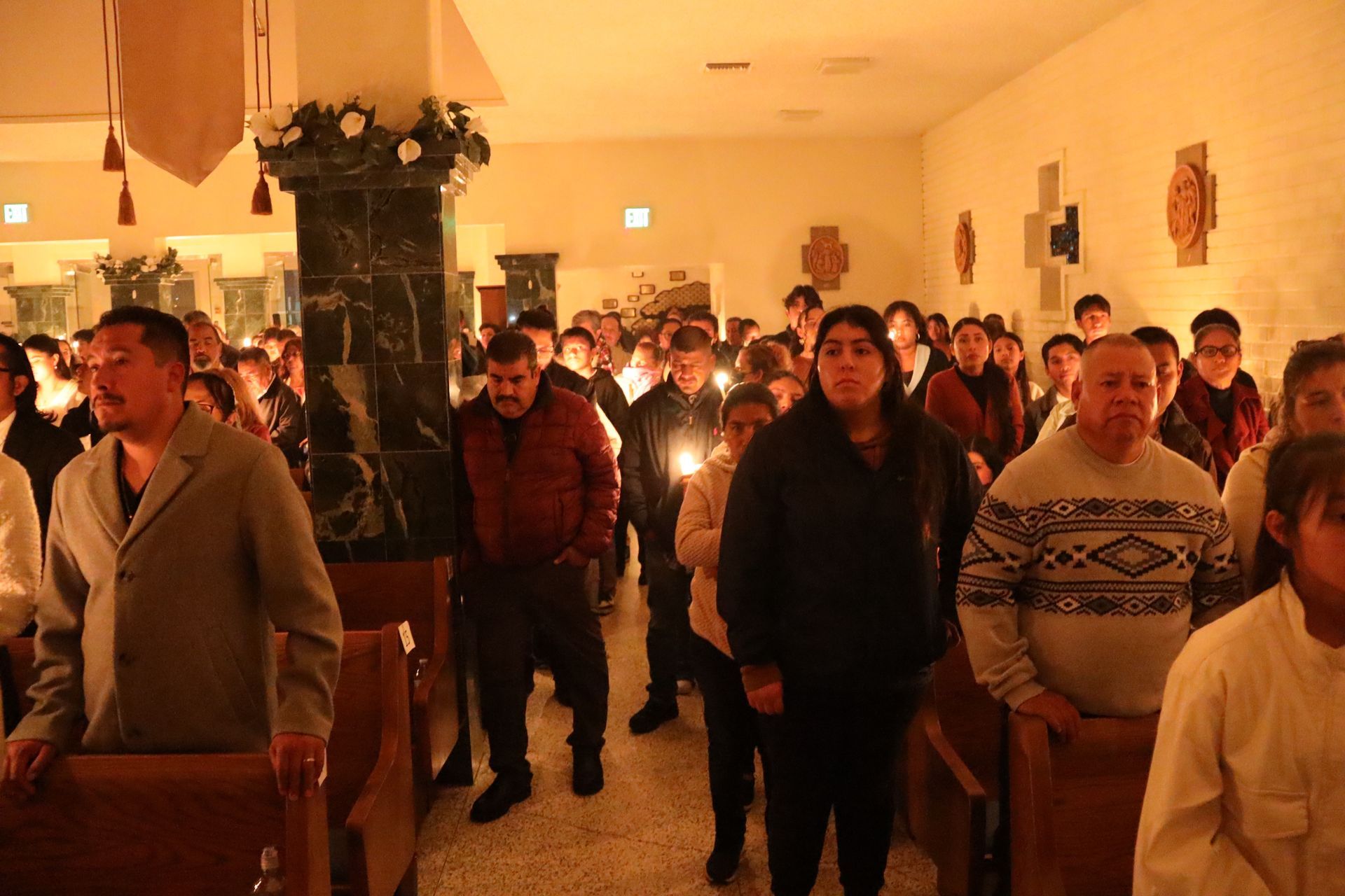 Crowd standing indoors in a warmly lit hall during a candlelight gathering