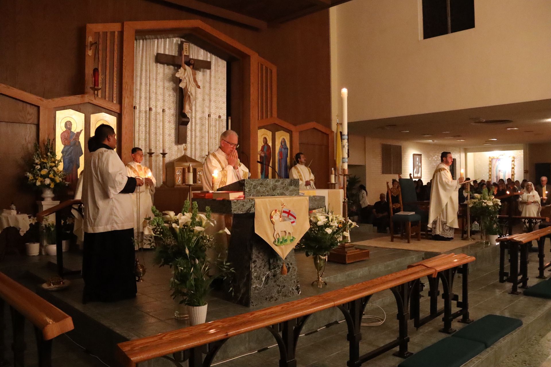 Catholic Mass in a church, with priests at the altar and a crucifix behind them.