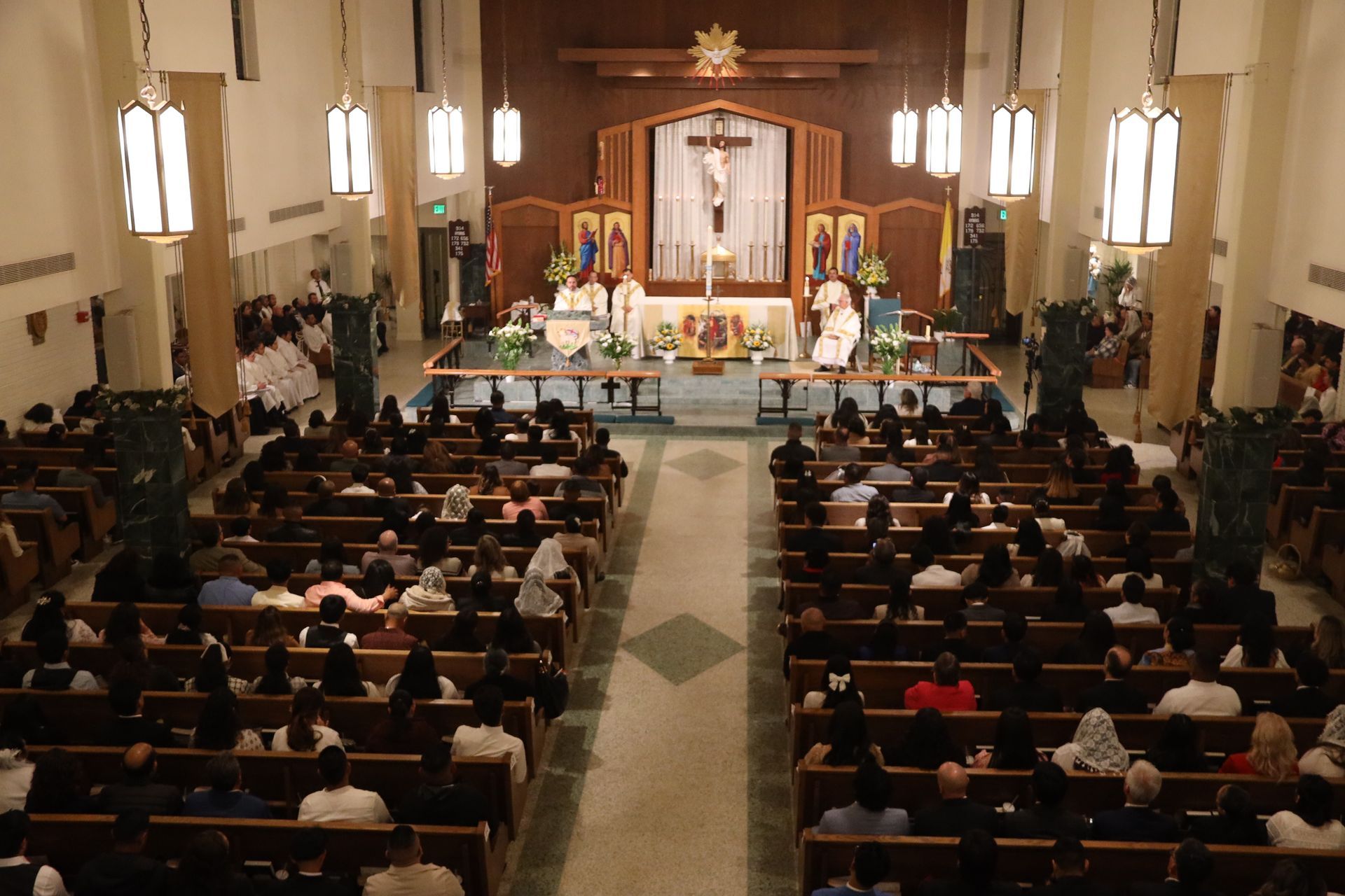 Packed church sanctuary with congregation seated in pews, facing a brightly lit altar during a service