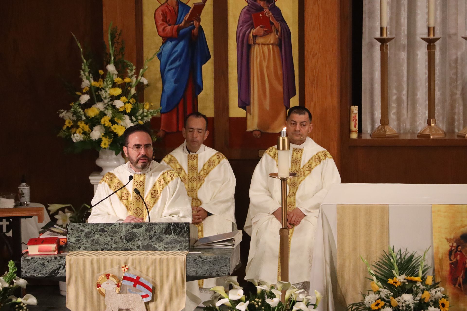 Three clergy in white and gold vestments stand at a church altar during a service.