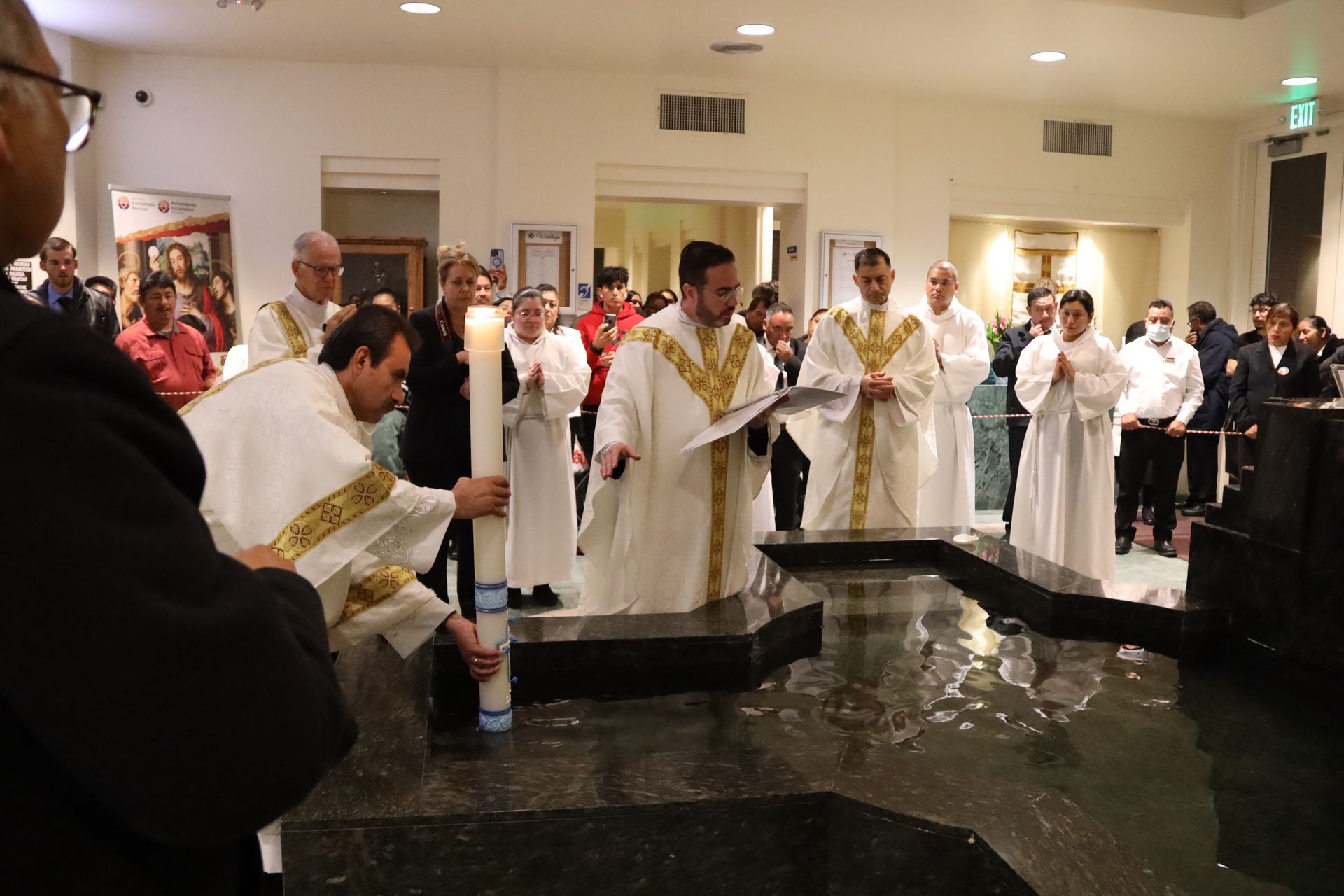Clergy in white robes standing around a baptismal font during a church ceremony
