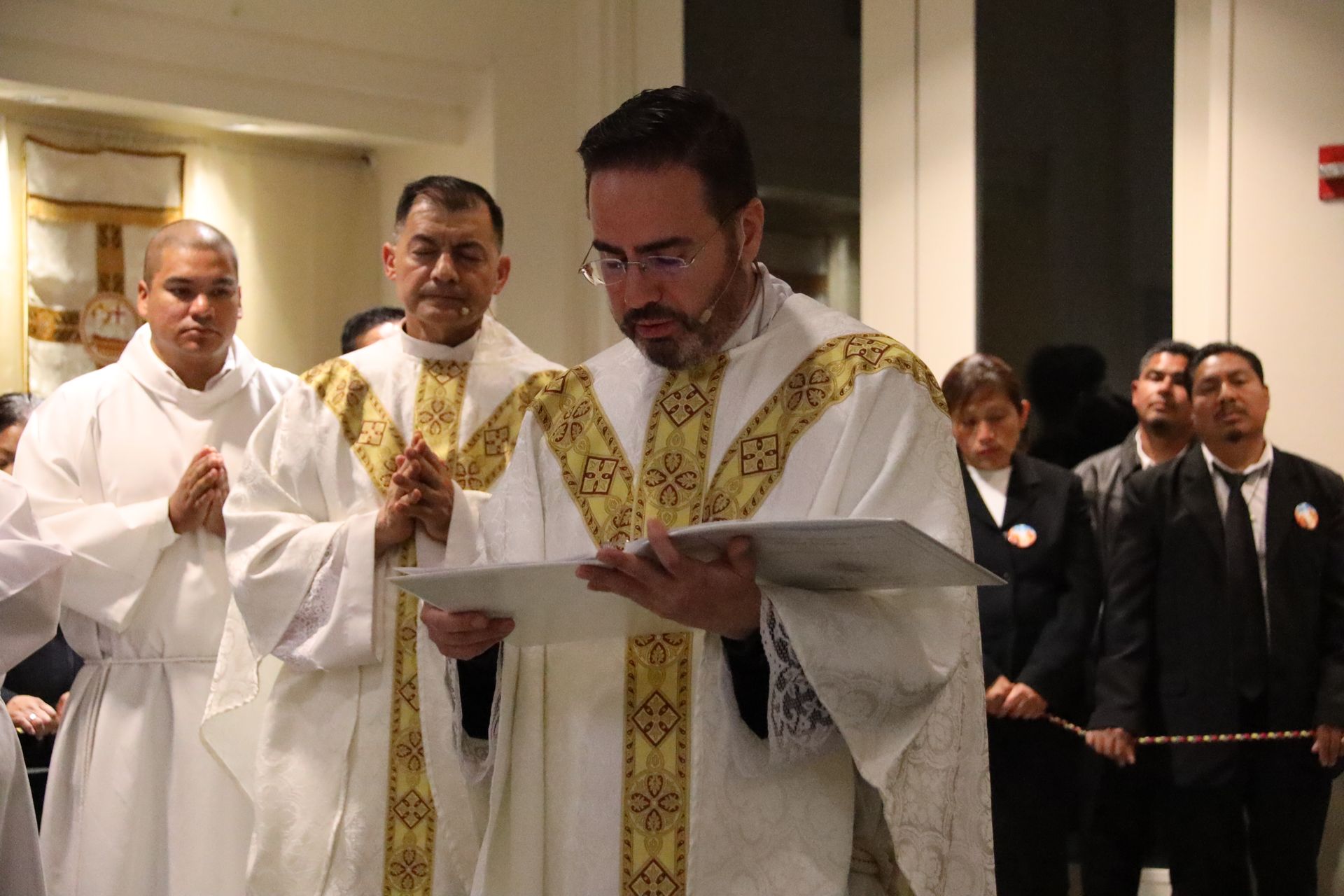 Clergy in white and gold robes reading from a book during a church ceremony