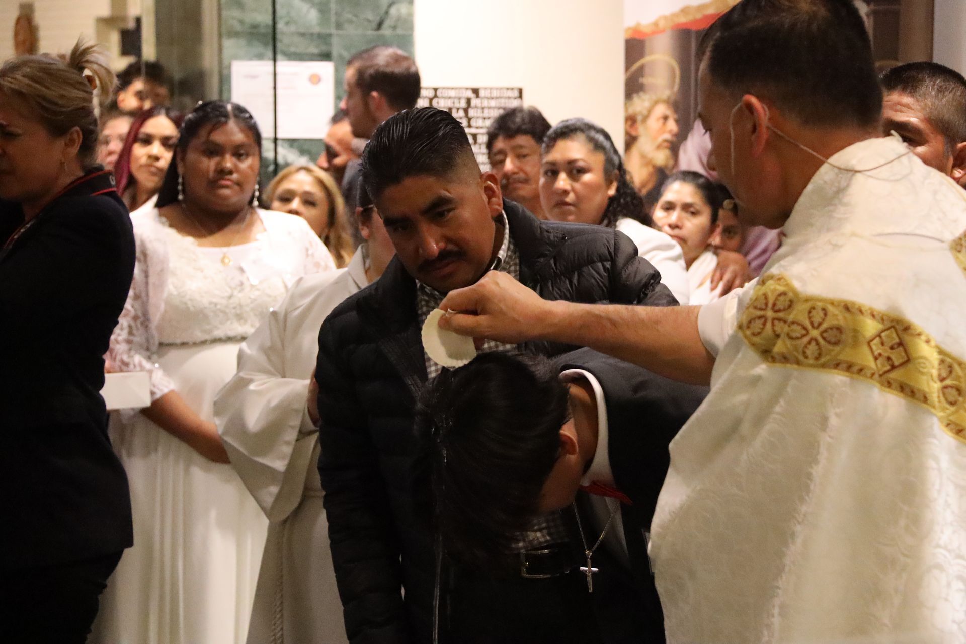 Priest anointing a man in a church ceremony while onlookers stand behind them