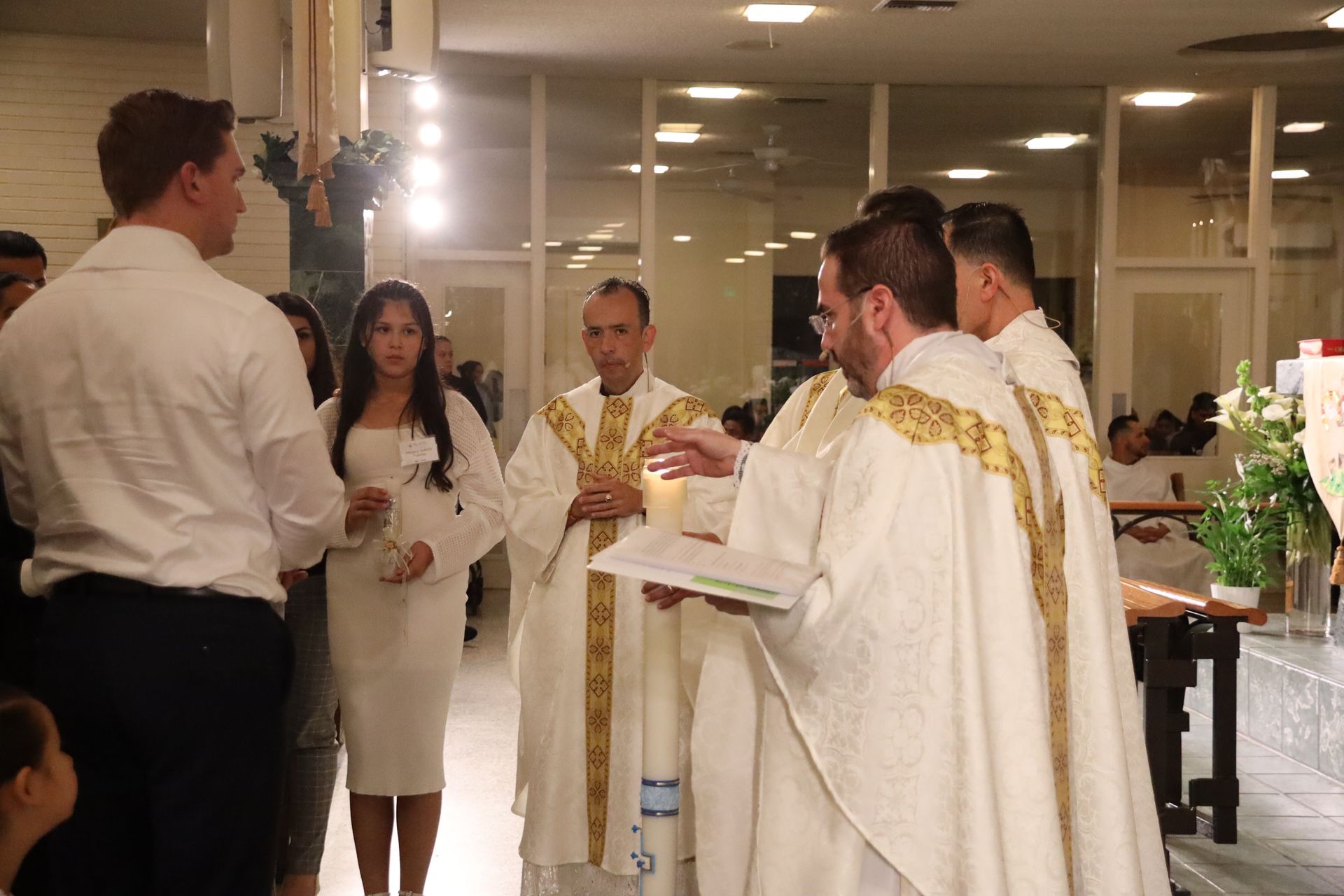 People in white and gold ceremonial robes stand indoors during a religious service.