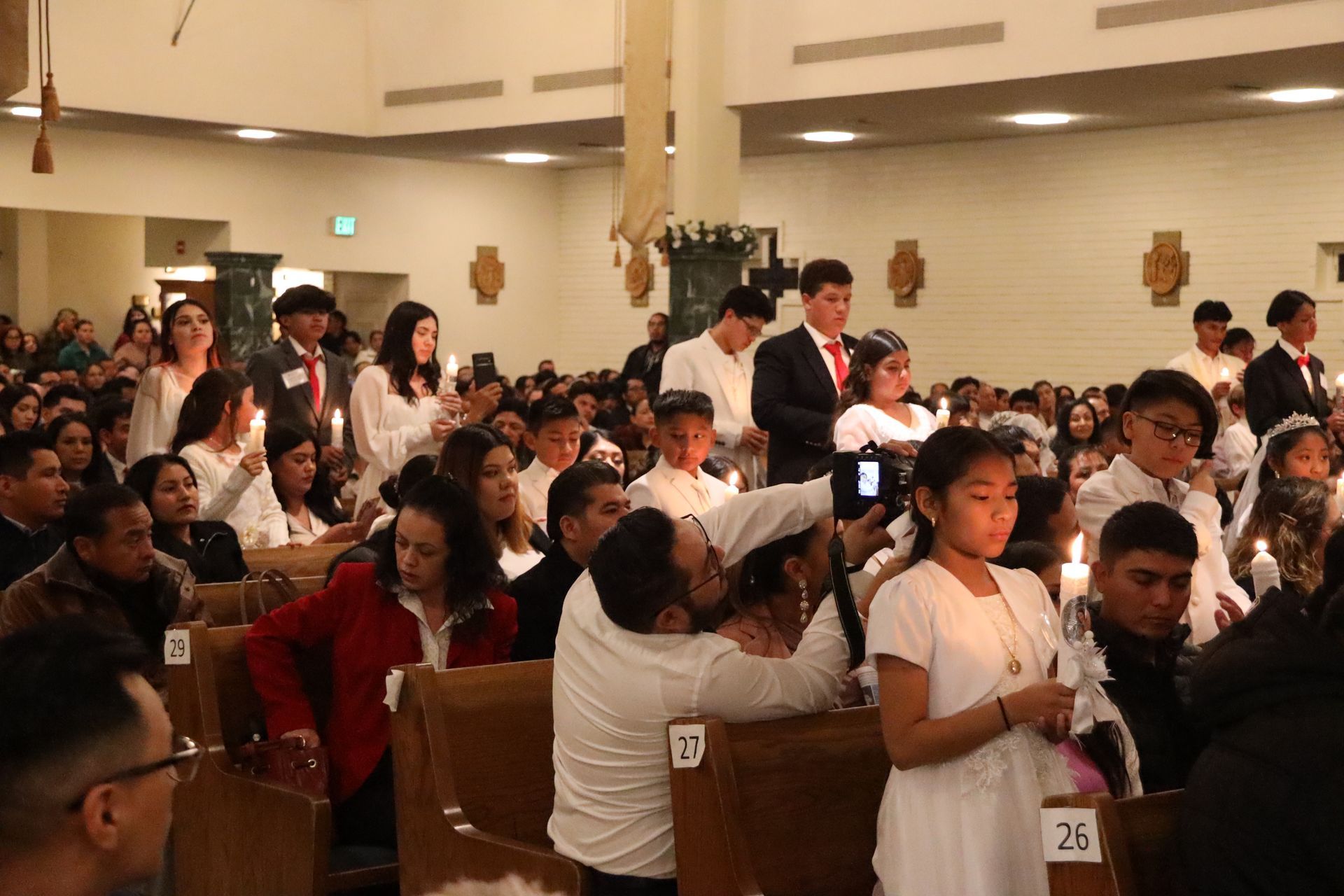 Congregation gathered in a church, many standing and holding lit candles during a ceremony.