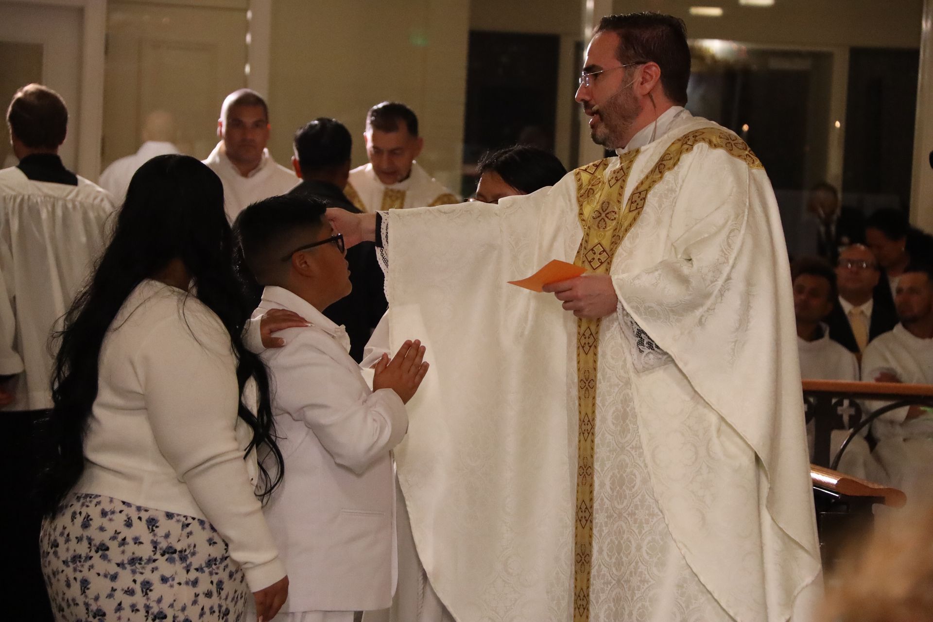 Priest in white vestments blessing two people kneeling in a church setting