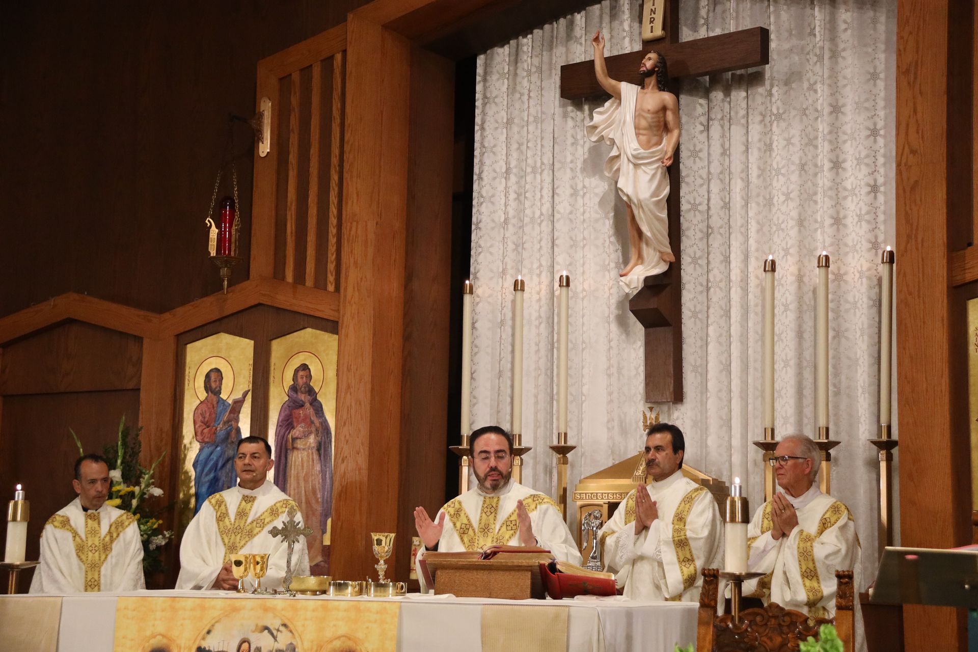 Priests in white vestments celebrate Mass at an altar beneath a crucifix in a church.