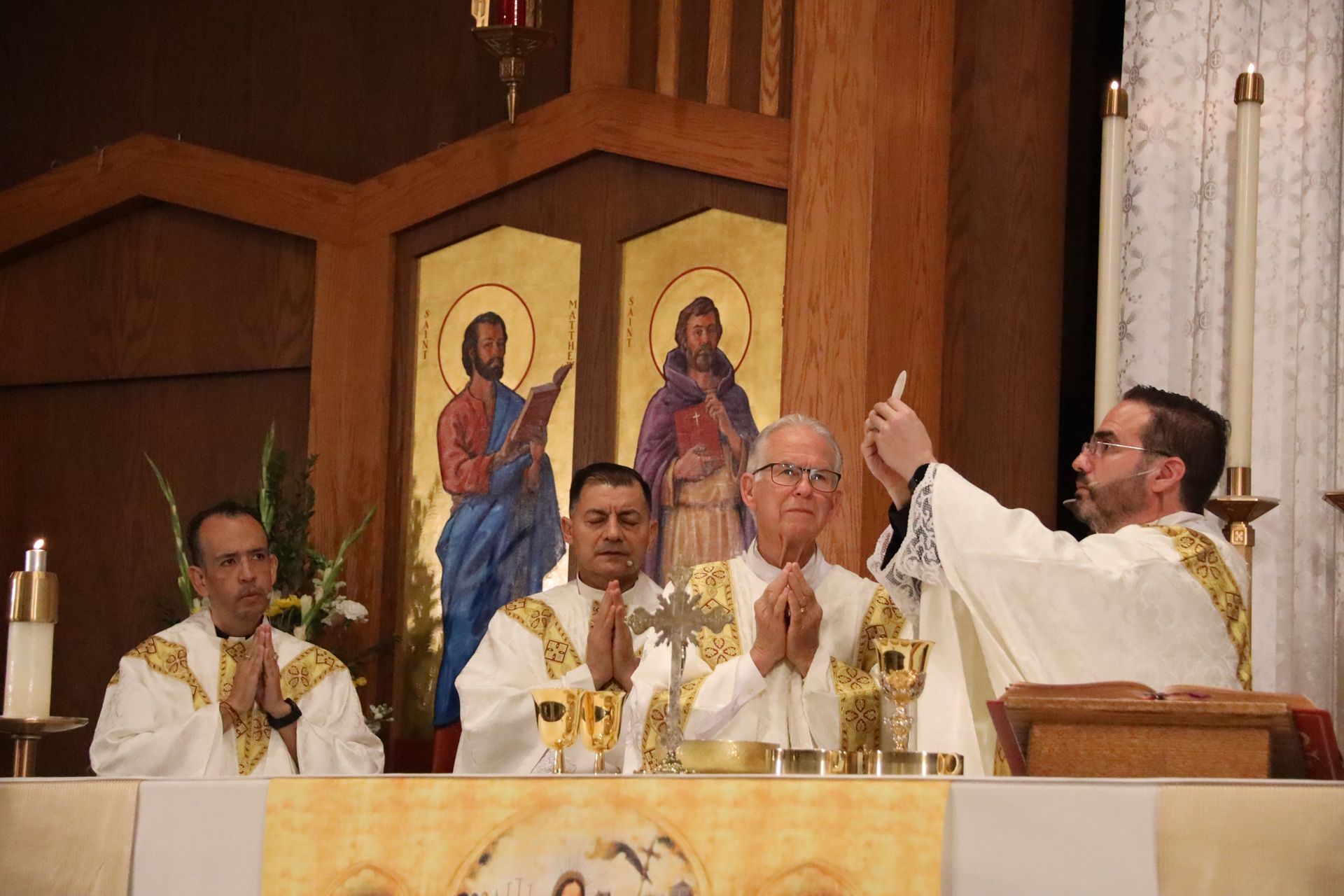 Catholic priests in white vestments celebrate Mass at an altar inside a church