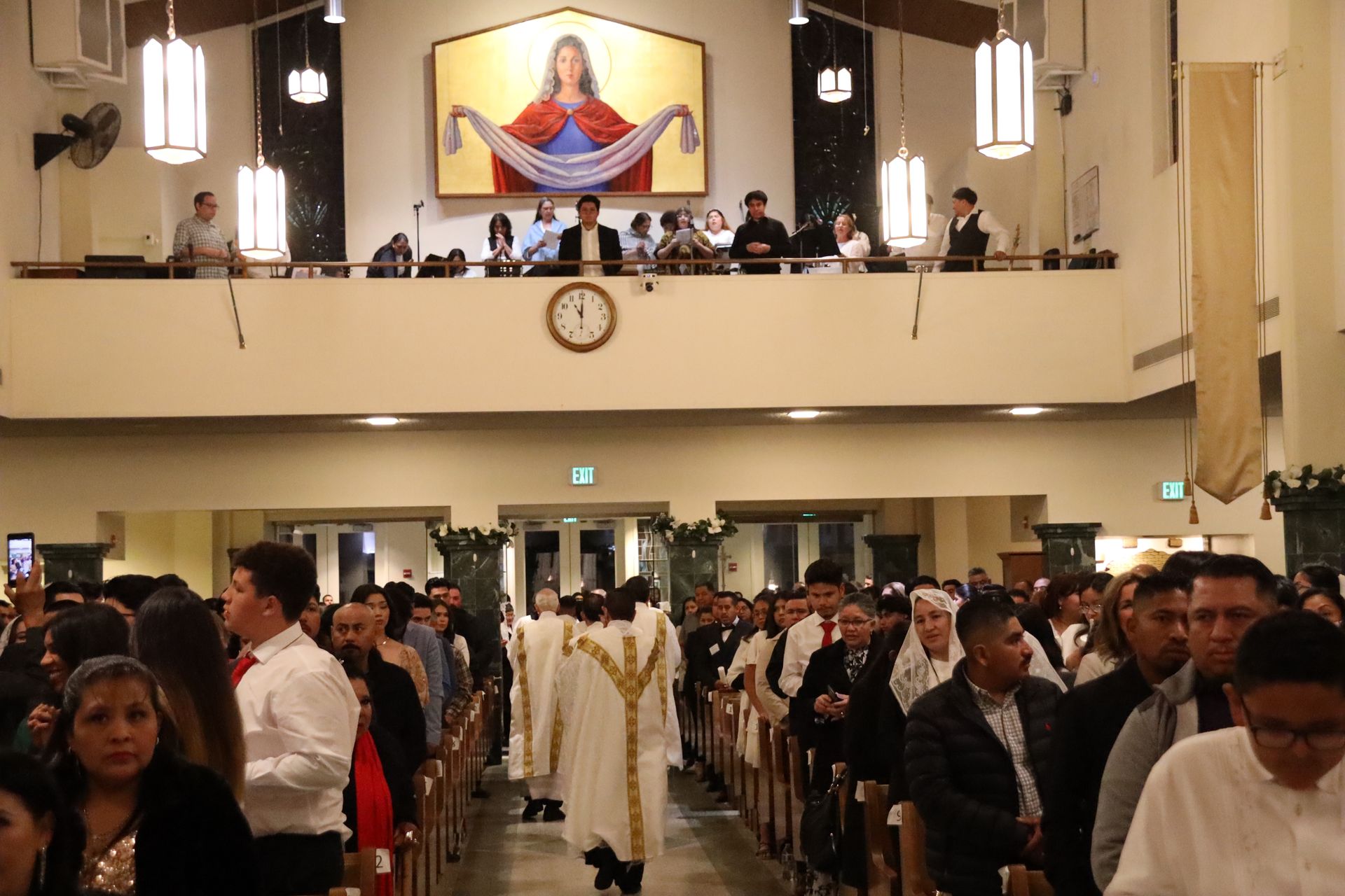 Congregation gathered in a church hall during a religious ceremony, with priests processing down the aisle.