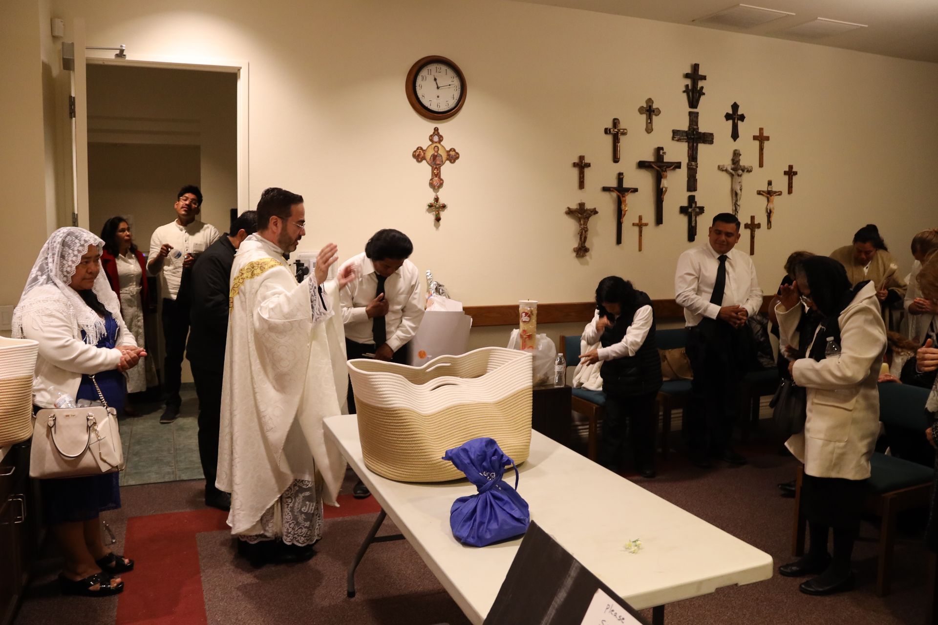 People gathered in a chapel-like room around a table of folded papers, with crosses on the wall.