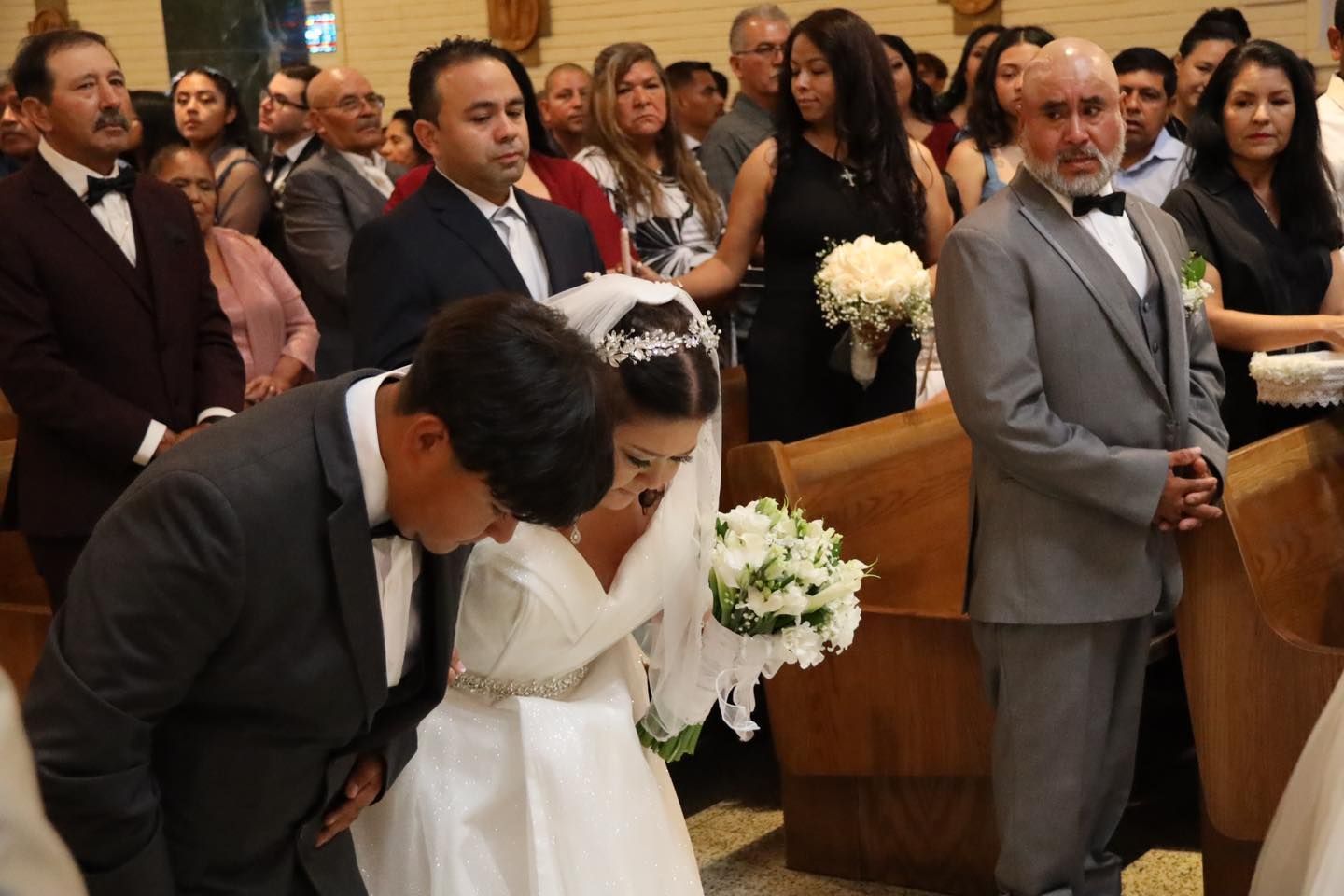 Wedding ceremony in a church, bride and groom bowing before a priest as guests watch.