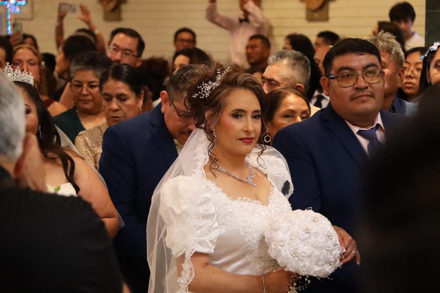 Bride in a white dress holding a bouquet, seated among guests at a wedding ceremony