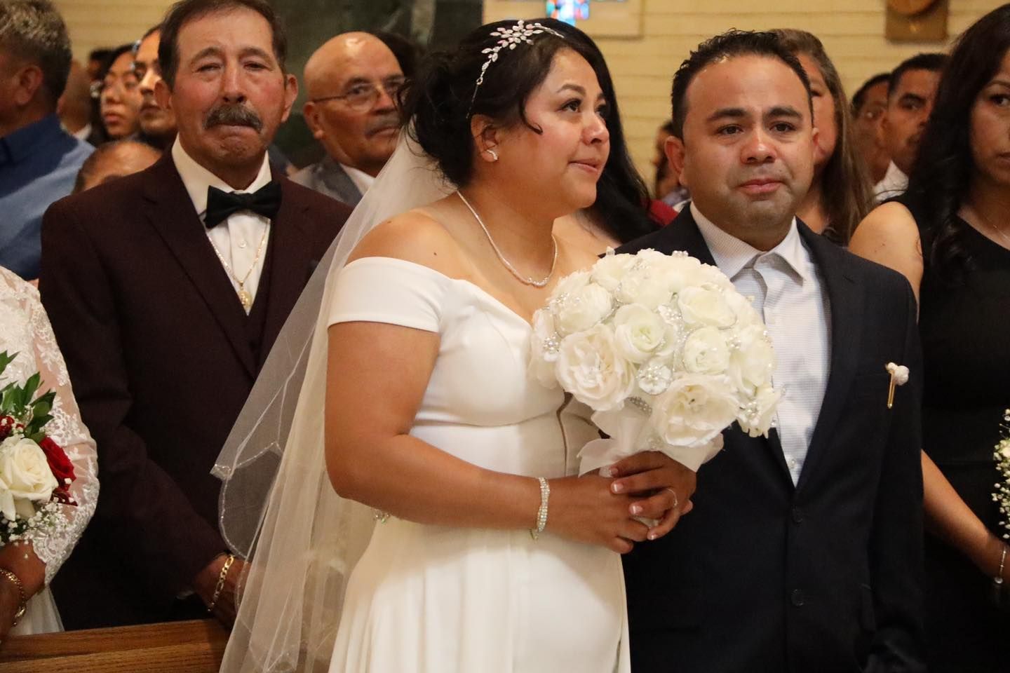 Bride in a white dress holds a bouquet at a wedding ceremony, standing beside a groom in a dark suit.