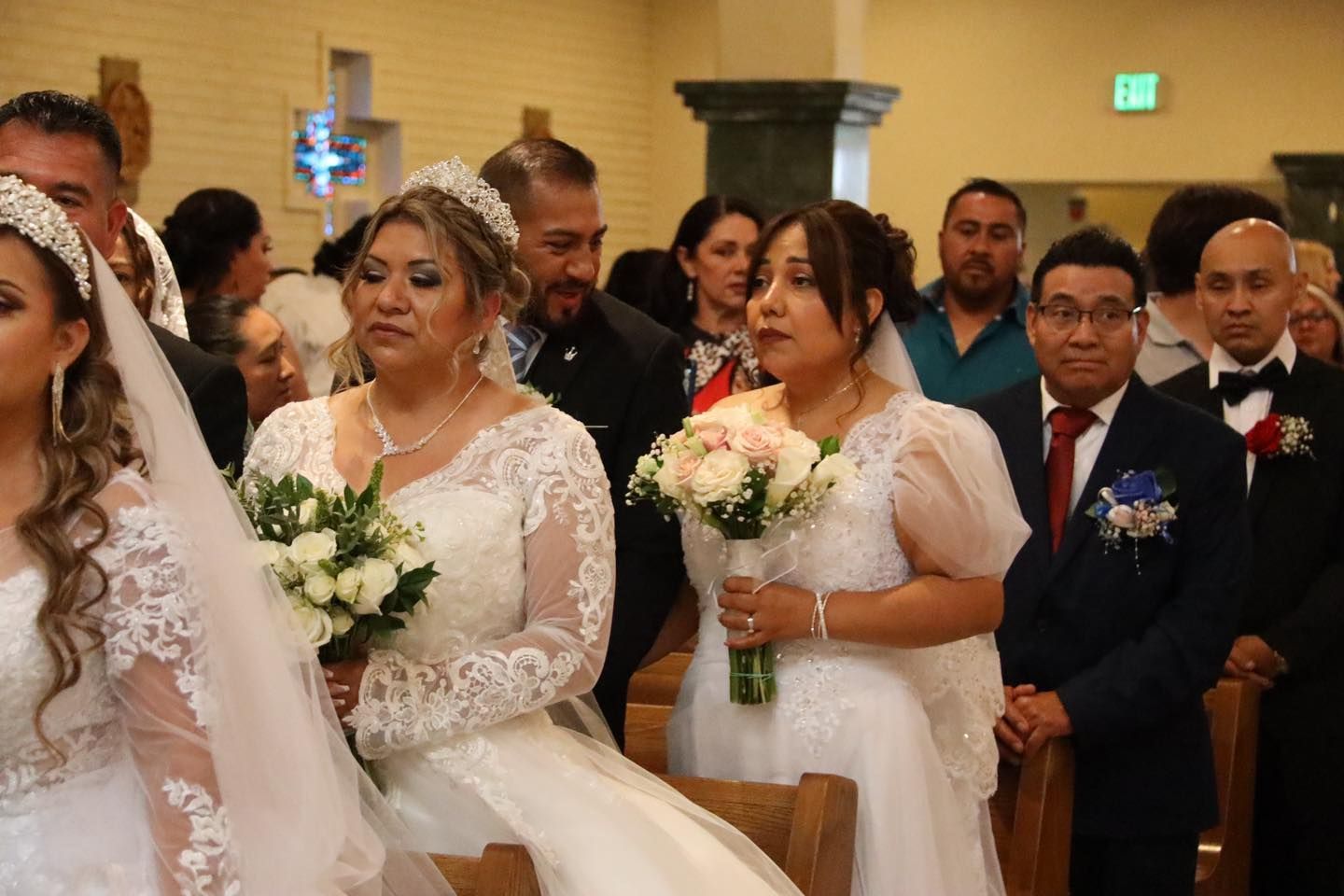 Bridal party seated in a church, holding white and peach bouquets during a wedding ceremony