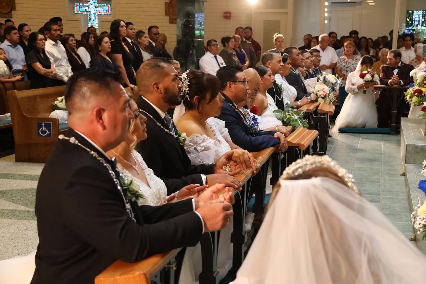 Wedding guests seated in a church, watching a ceremony with the bride at the front.
