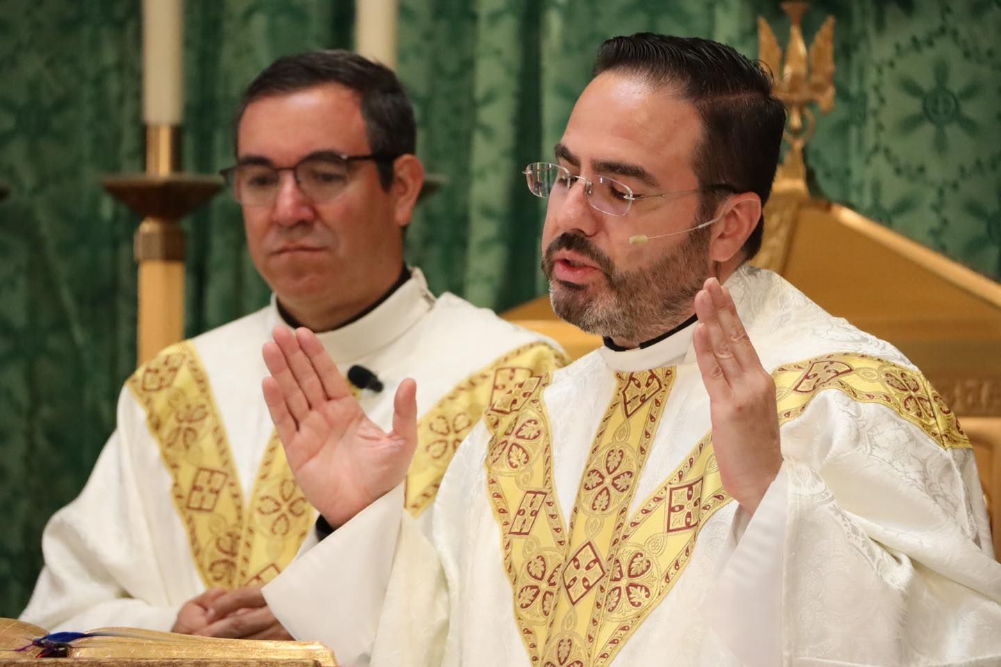 Two priests in white and gold vestments speaking during a church service