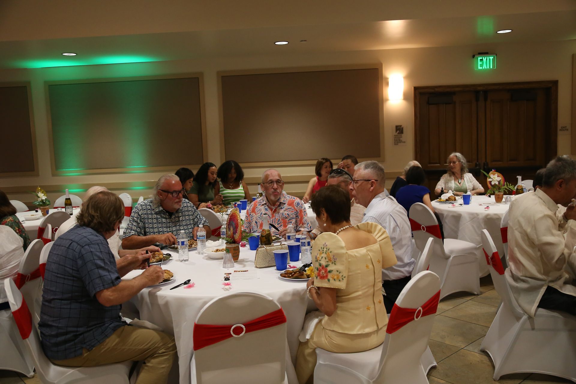 People seated at round banquet tables in a warmly lit conference room, eating and talking.