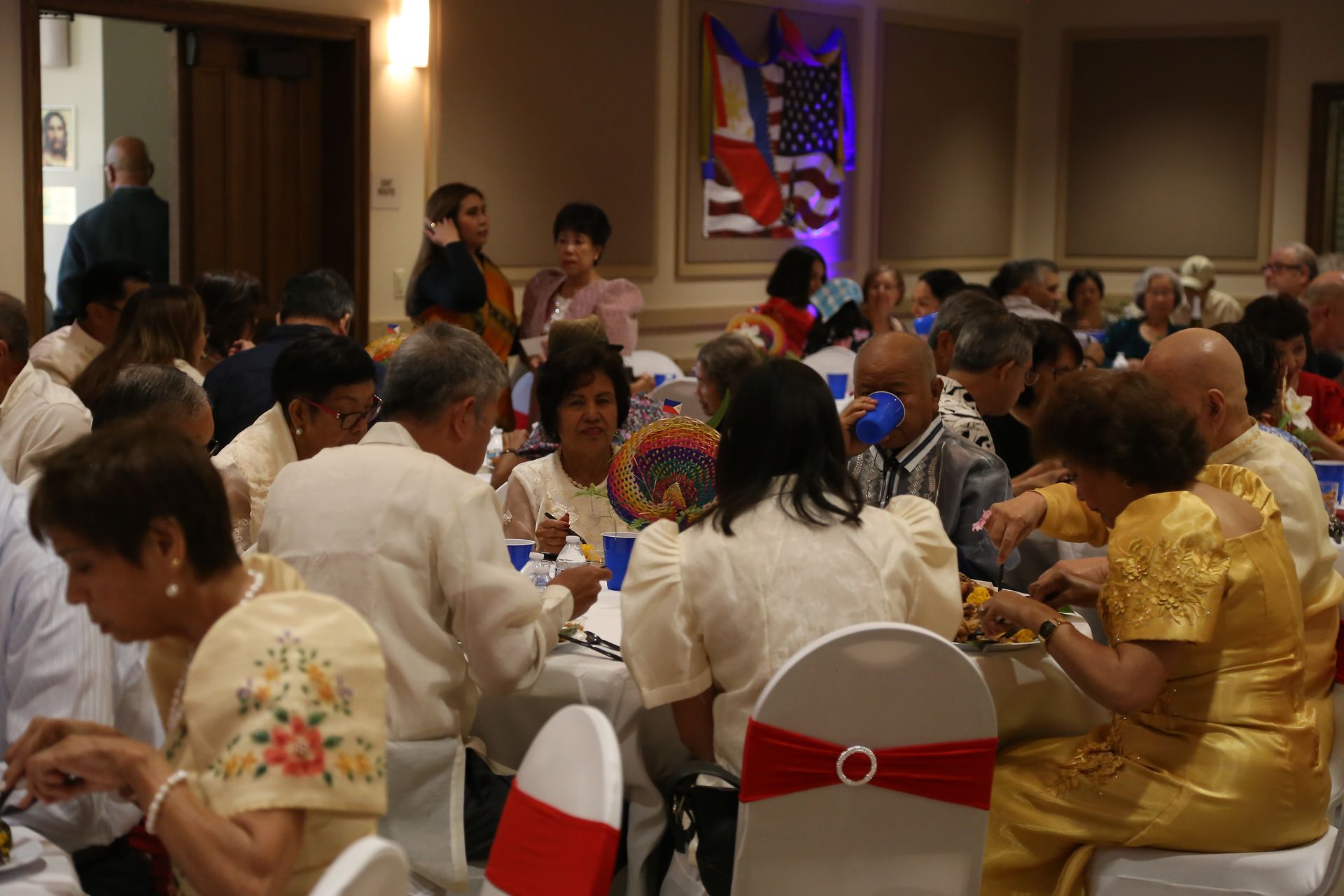 People seated at round tables in a banquet hall, dining and chatting under warm lighting.